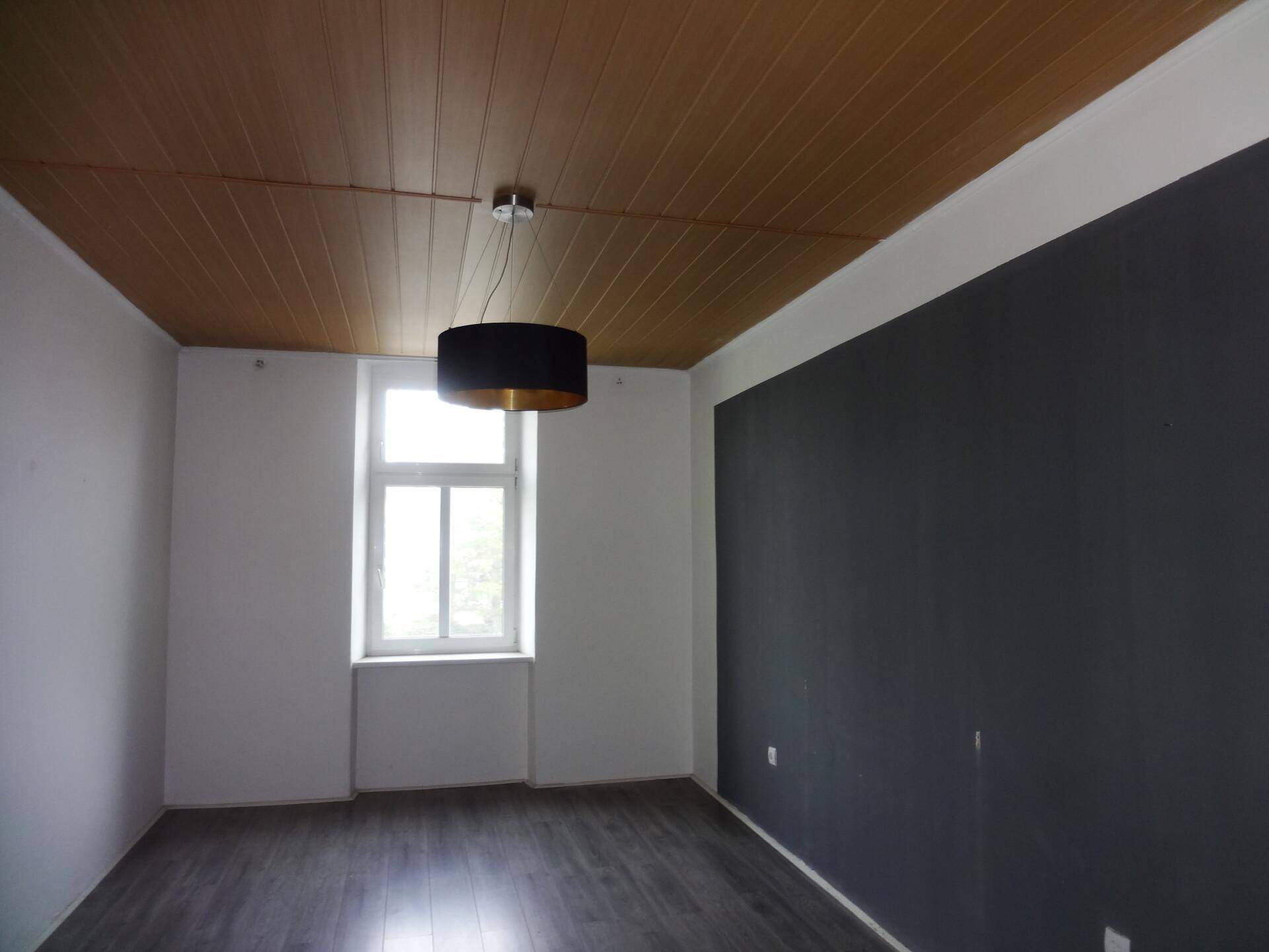 Zimmer mit dunkler Akzentwand, Holzpaneeldecke und einem Fenster.