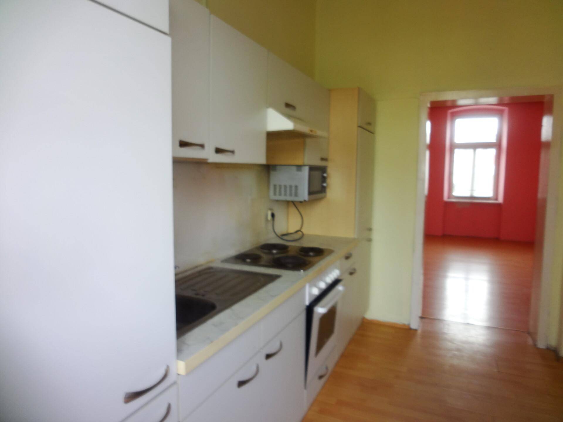 Kleine Küche mit gelben Wänden, Einbauschränken und Blick in ein angrenzendes Zimmer.