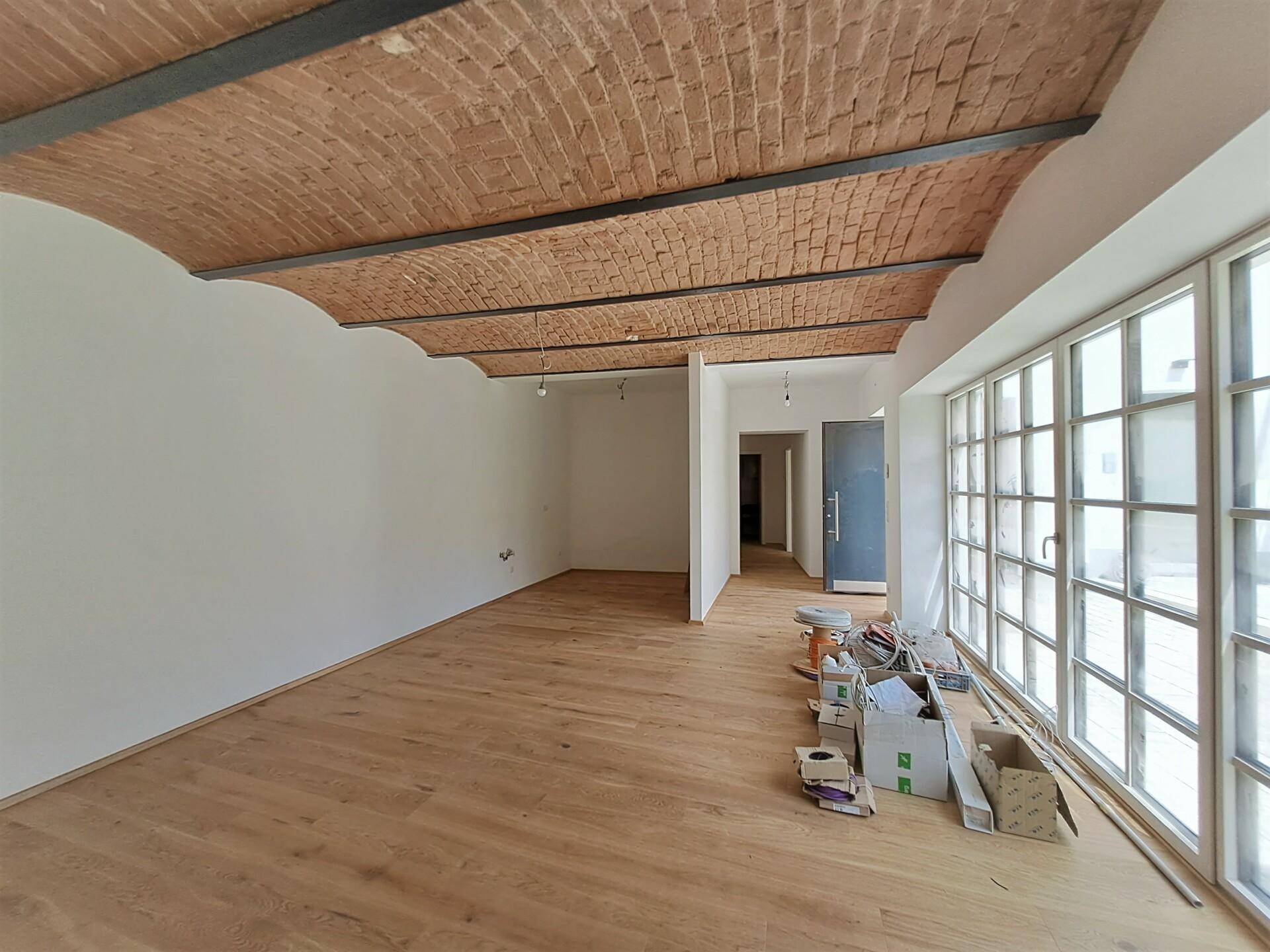 Heller Raum mit Holzboden, Ziegelgewölbedecke und großen Fenstern, noch im Bauzustand.