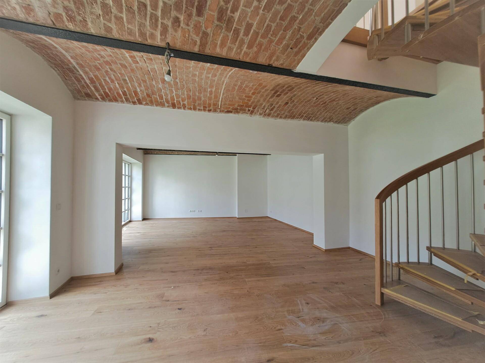 Großer Raum mit Holzboden, Ziegelgewölbedecke und einer eleganten Wendeltreppe.