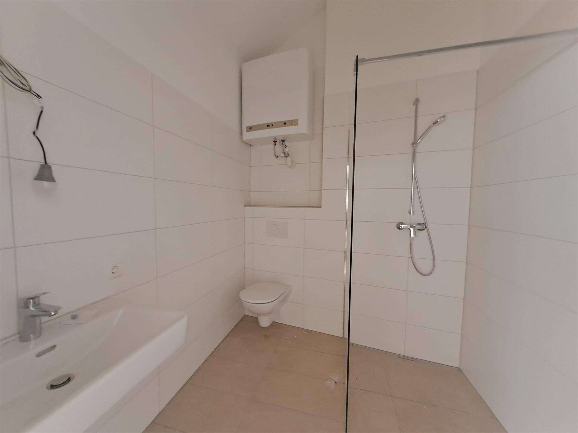 Modernes Badezimmer mit weißen Fliesen, Duschbereich, WC, Waschbecken und Warmwasserbereiter.