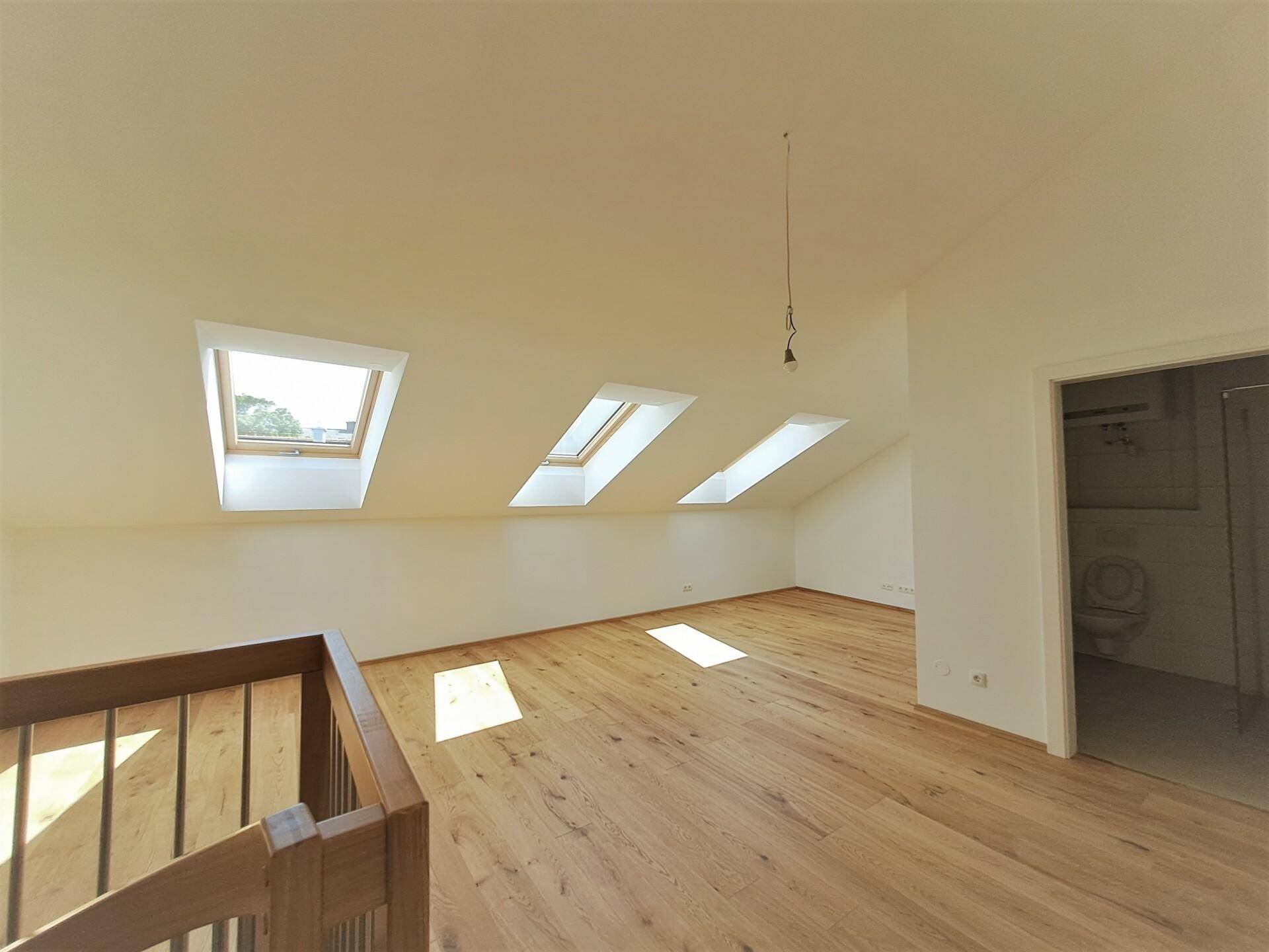 Geräumiger Dachraum mit Holzboden, schrägen Wänden und mehreren Dachfenstern.