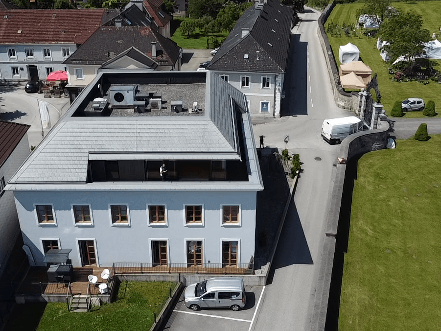 Luftaufnahme eines modernen Gebäudes mit Dachterrasse und umliegender Landschaft.