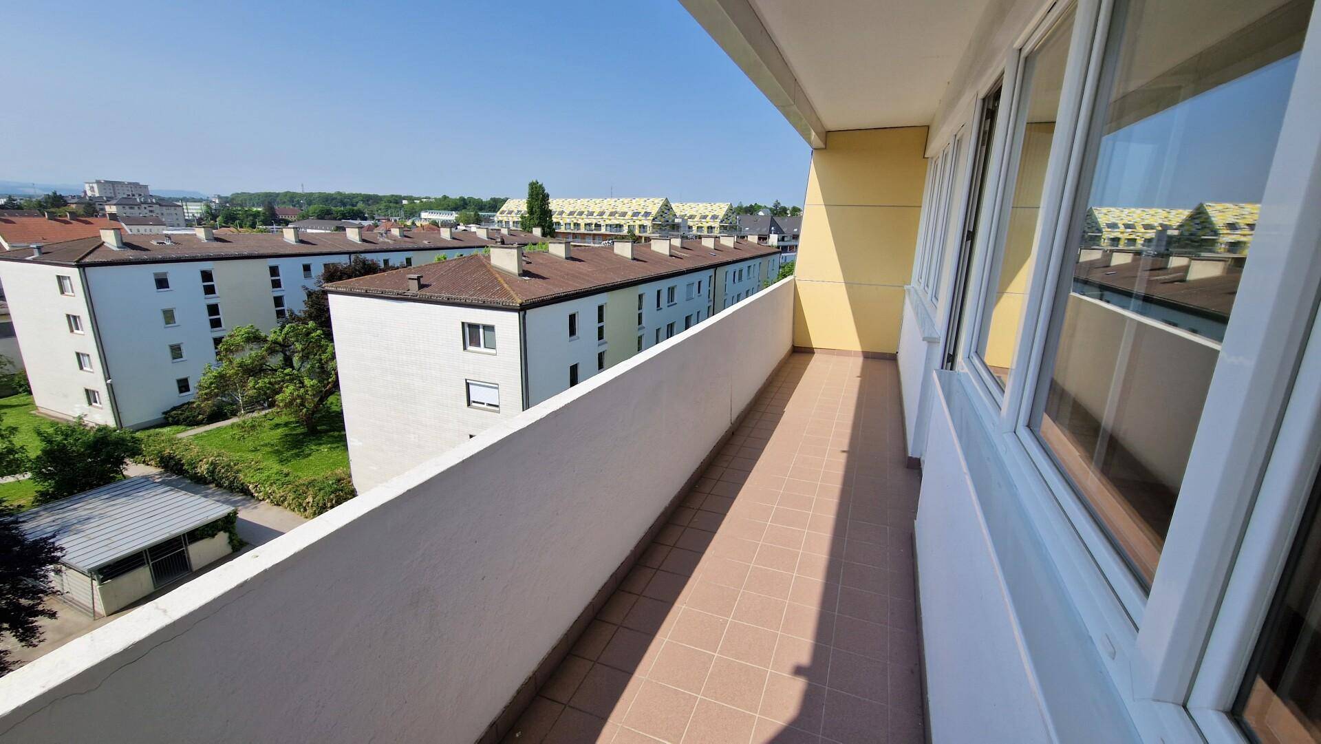 Langer Balkon mit Fliesenboden und Blick auf die umliegenden Gebäude und Grünflächen.