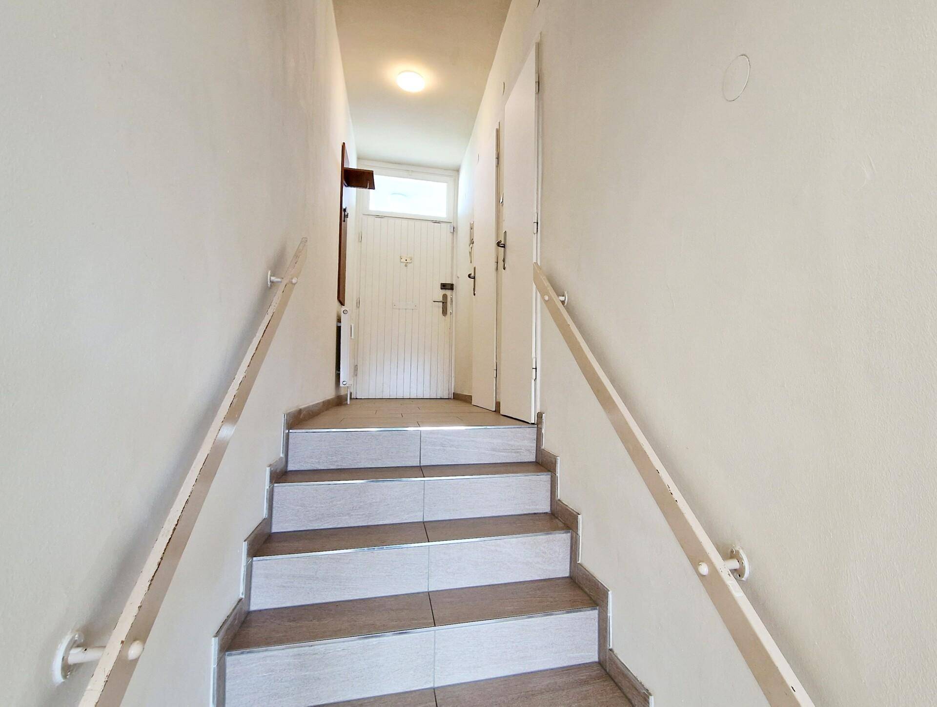 Treppenhaus mit Fliesenboden und Handläufen, das zum Eingangsbereich führt.