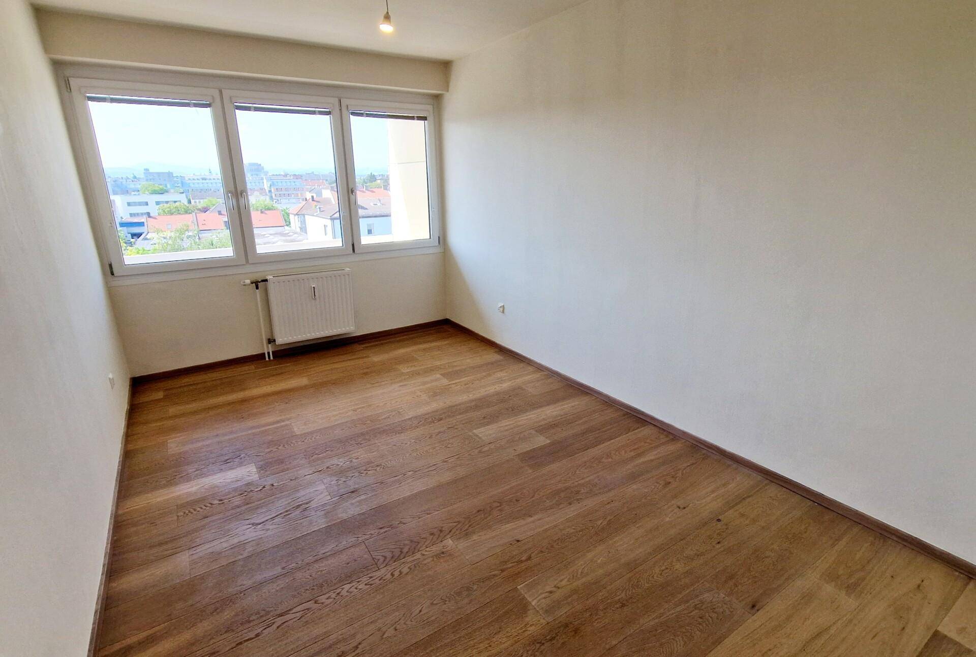 Helles Zimmer mit Parkettboden und großen Fenstern, die einen weiten Blick bieten.