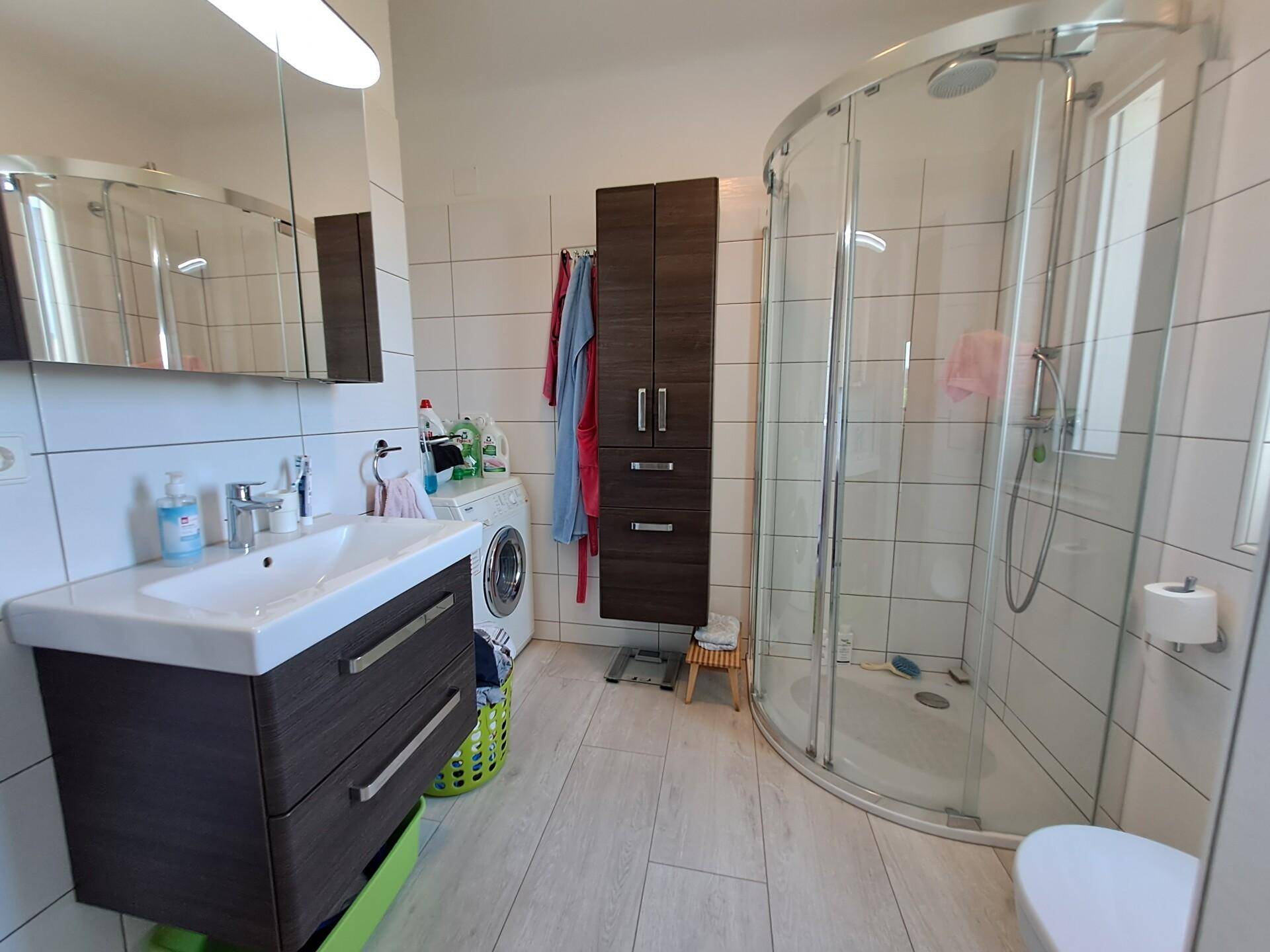 Modernes Badezimmer mit Dusche, Waschbecken, WC und integrierter Waschmaschine.