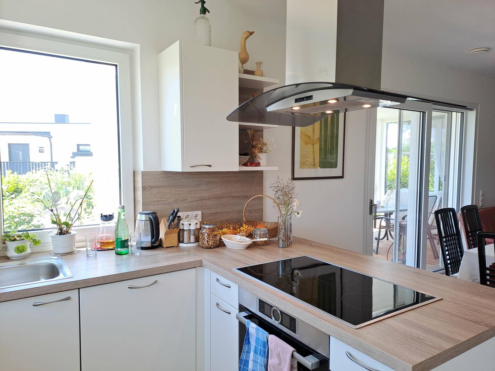 Moderne Einbauküche mit Induktionskochfeld, Dunstabzugshaube und Arbeitsplatten in Holzoptik.