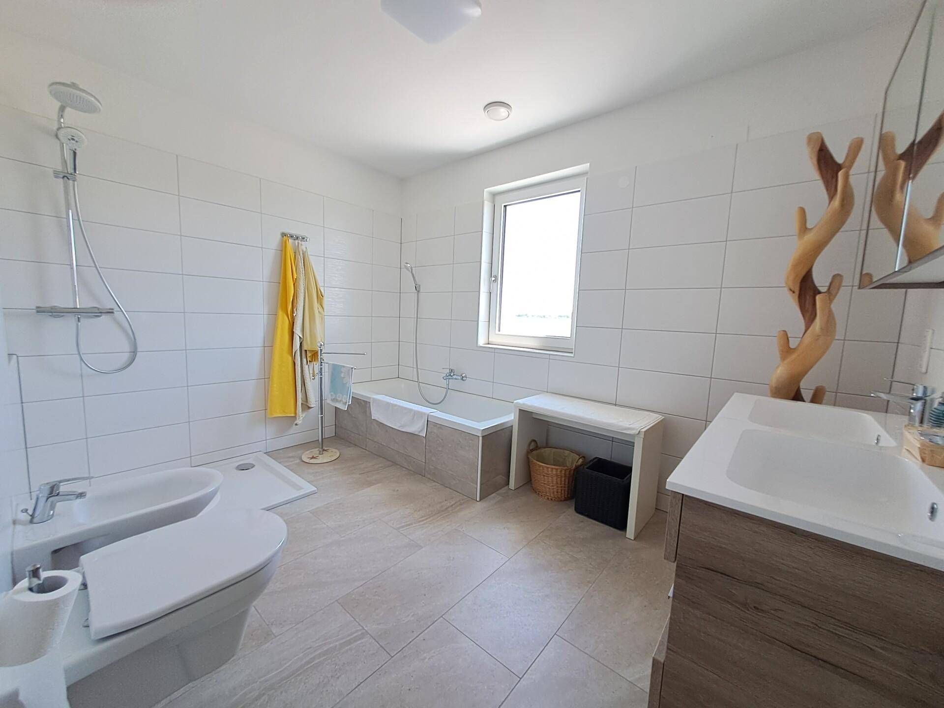 Geräumiges Badezimmer mit Badewanne, Dusche, Doppelwaschbecken und einem Fenster für Tageslicht.