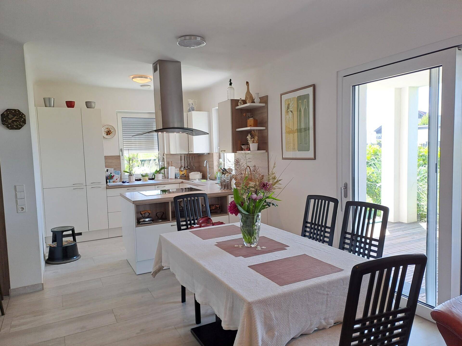 Offene, moderne Küche mit Essbereich, Kochinsel und direktem Zugang zur sonnigen Terrasse.