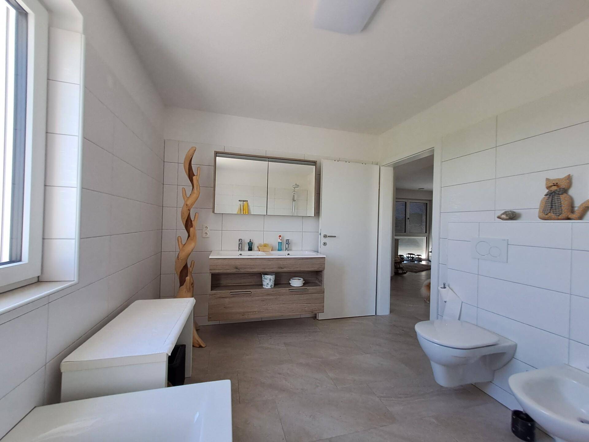 Helles Badezimmer mit Doppelwaschbecken, wandhängendem WC, Bidet und großem Spiegelschrank.