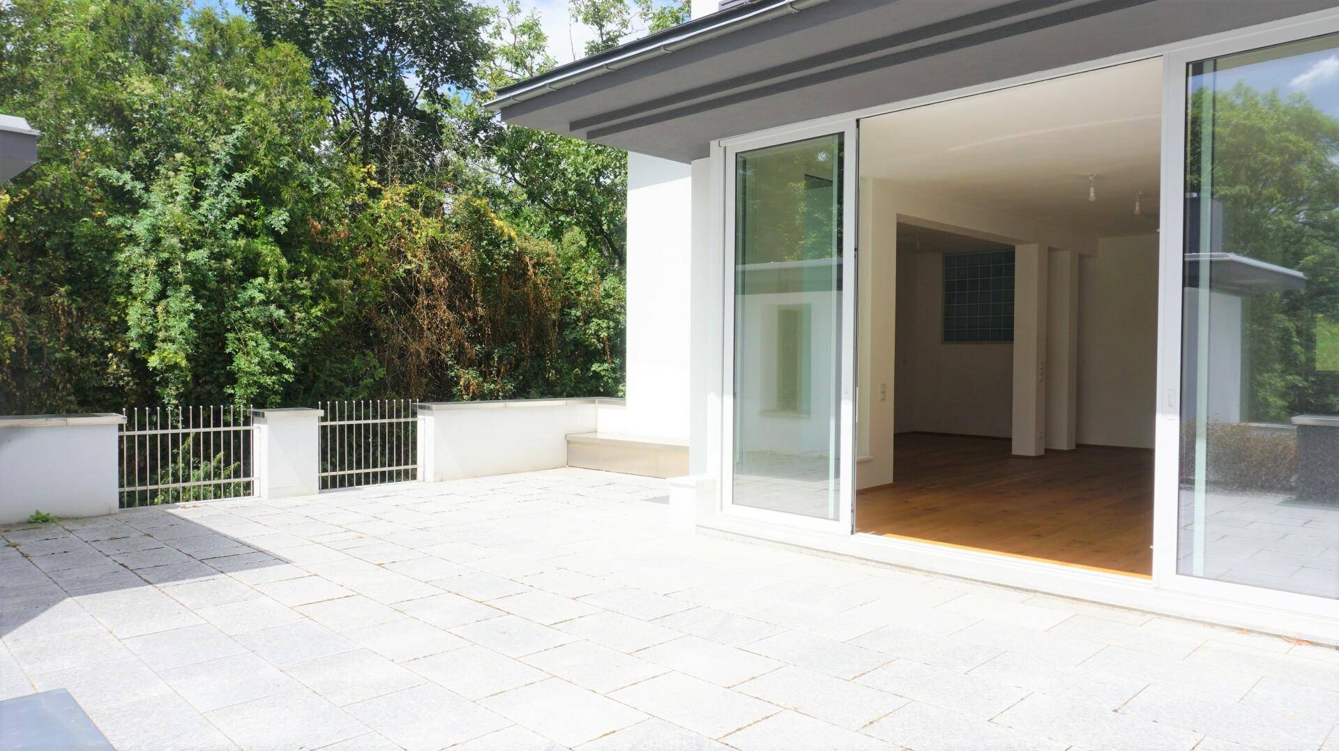 Heller Wohnraum mit Holzboden und großen Schiebetüren, die zu einer geräumigen Terrasse führen.