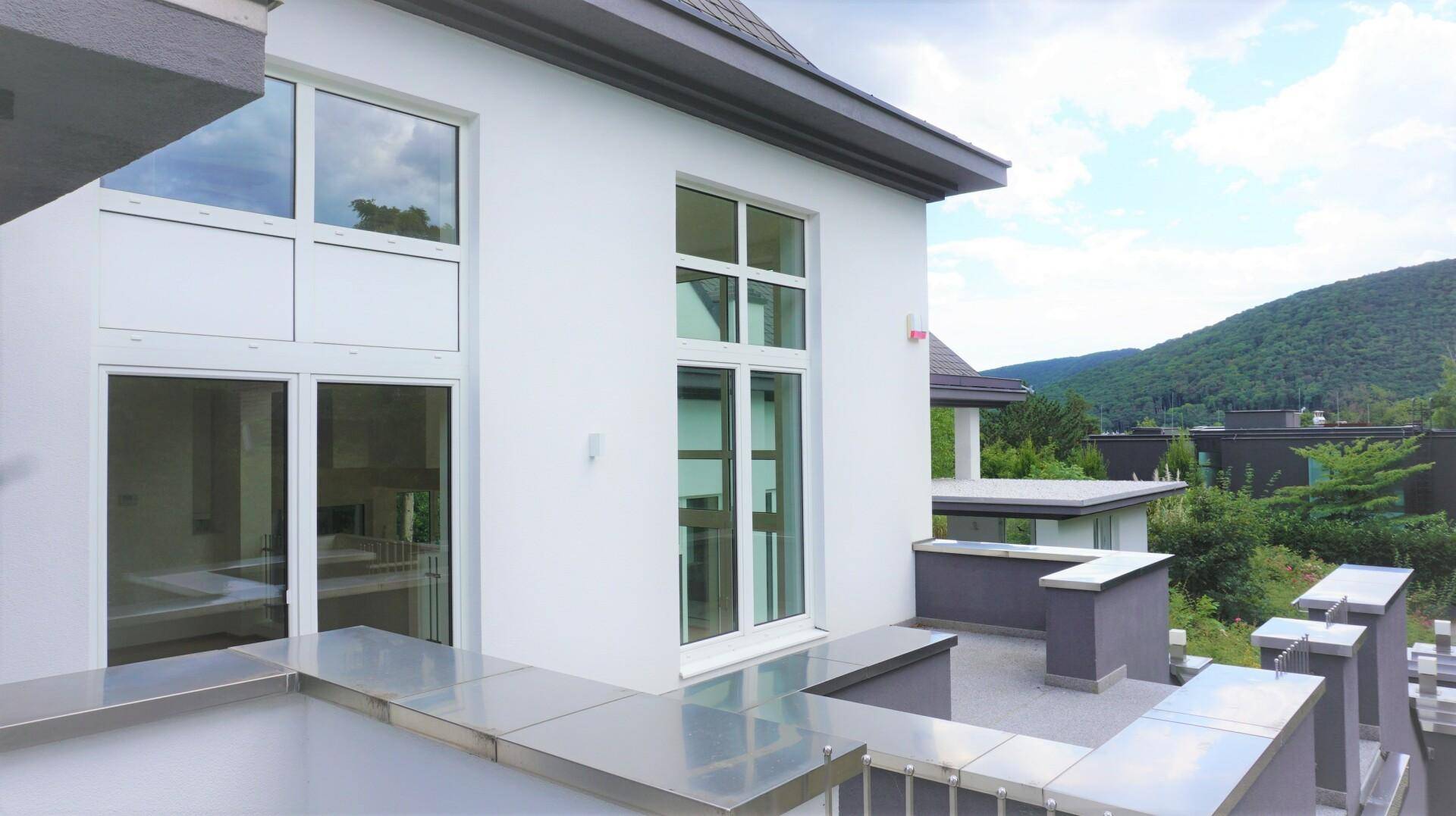 Weiße Fassade mit großen Fenstern und einem schmalen Balkon mit Blick auf die grüne Umgebung.