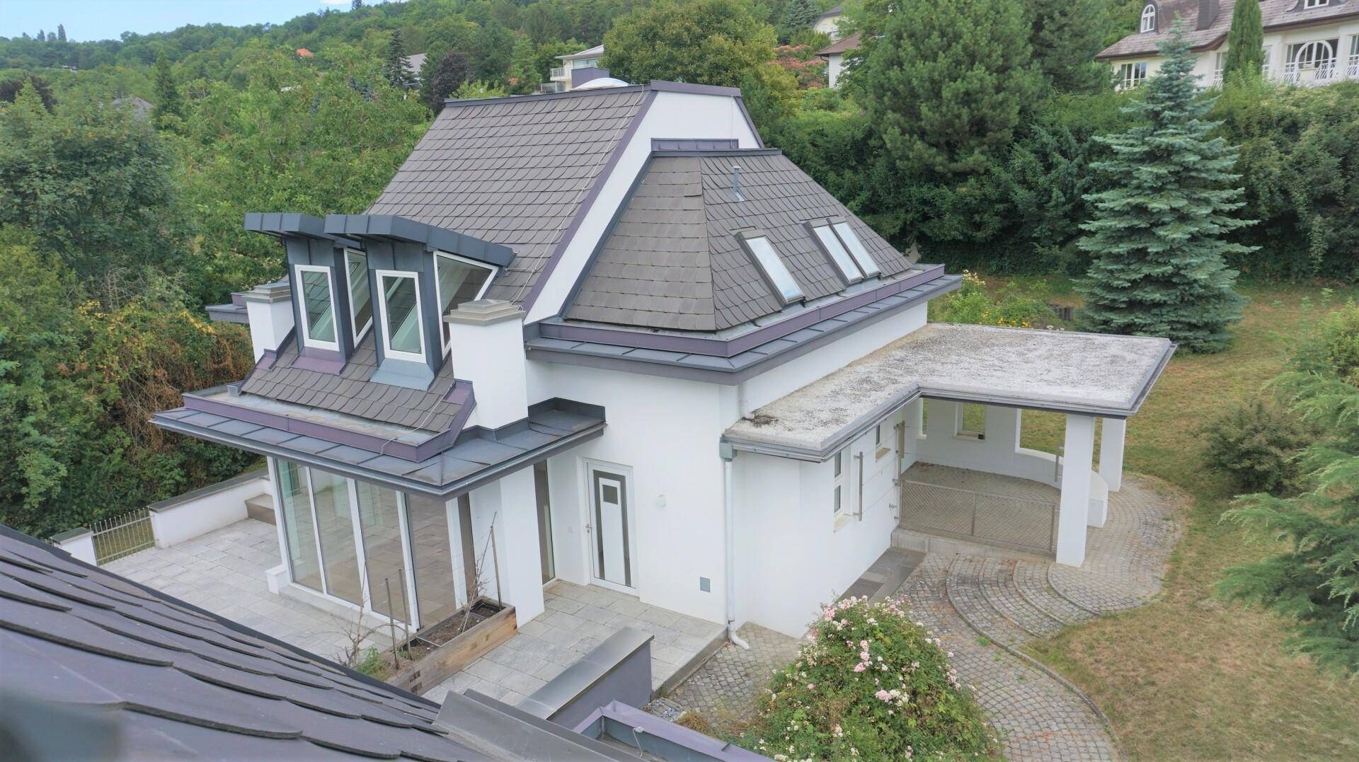 Vogelperspektive einer modernen Villa mit Satteldach, Gauben und angrenzendem Carport.