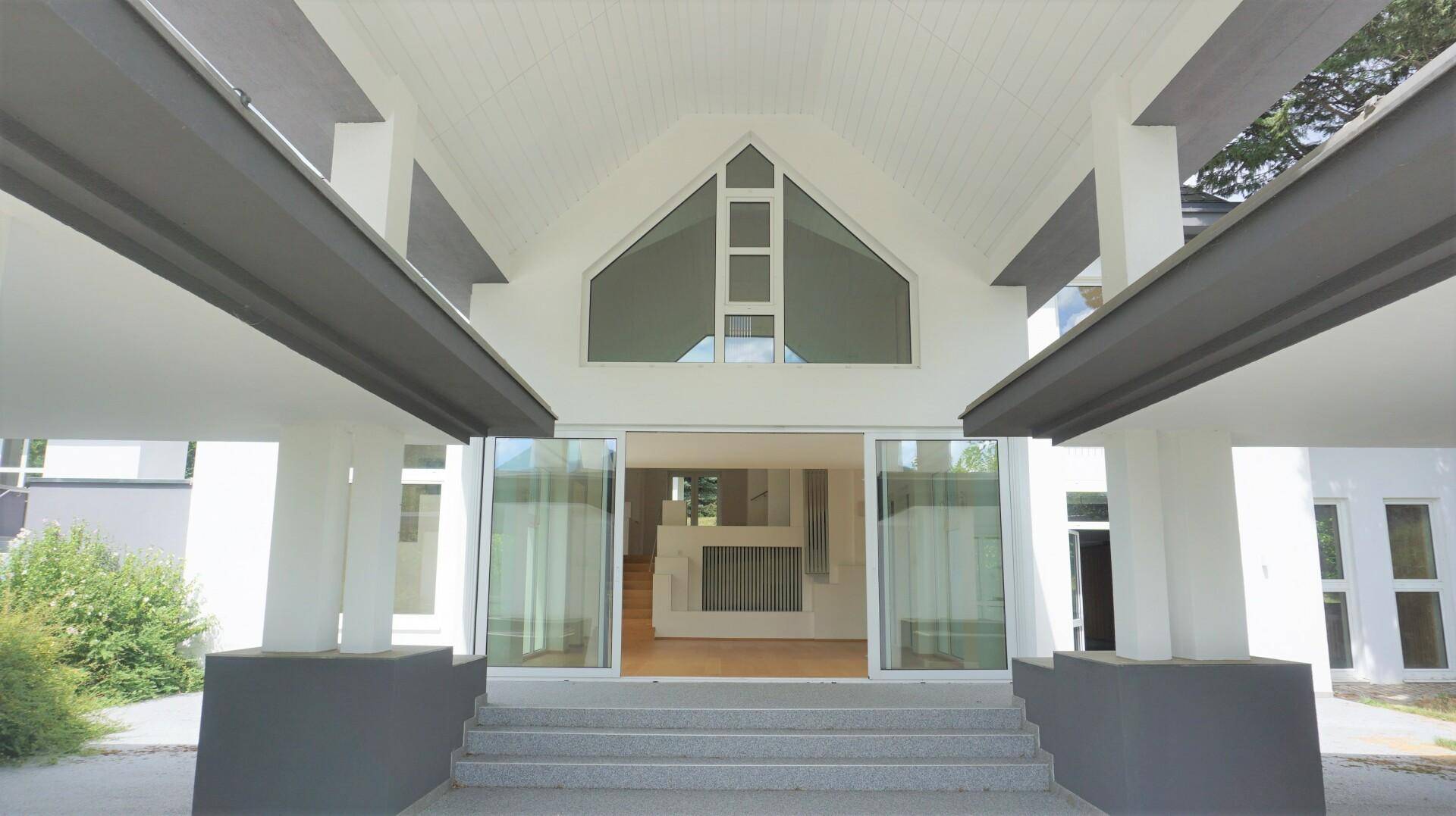 Repräsentativer Eingangsbereich der Villa mit hohen Säulen und großen Glasfronten.