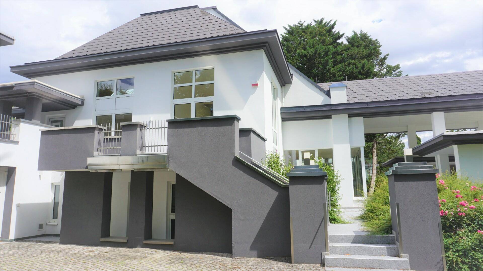 Seitliche Ansicht der Villa mit Außentreppe und Balkon, umgeben von grüner Bepflanzung.