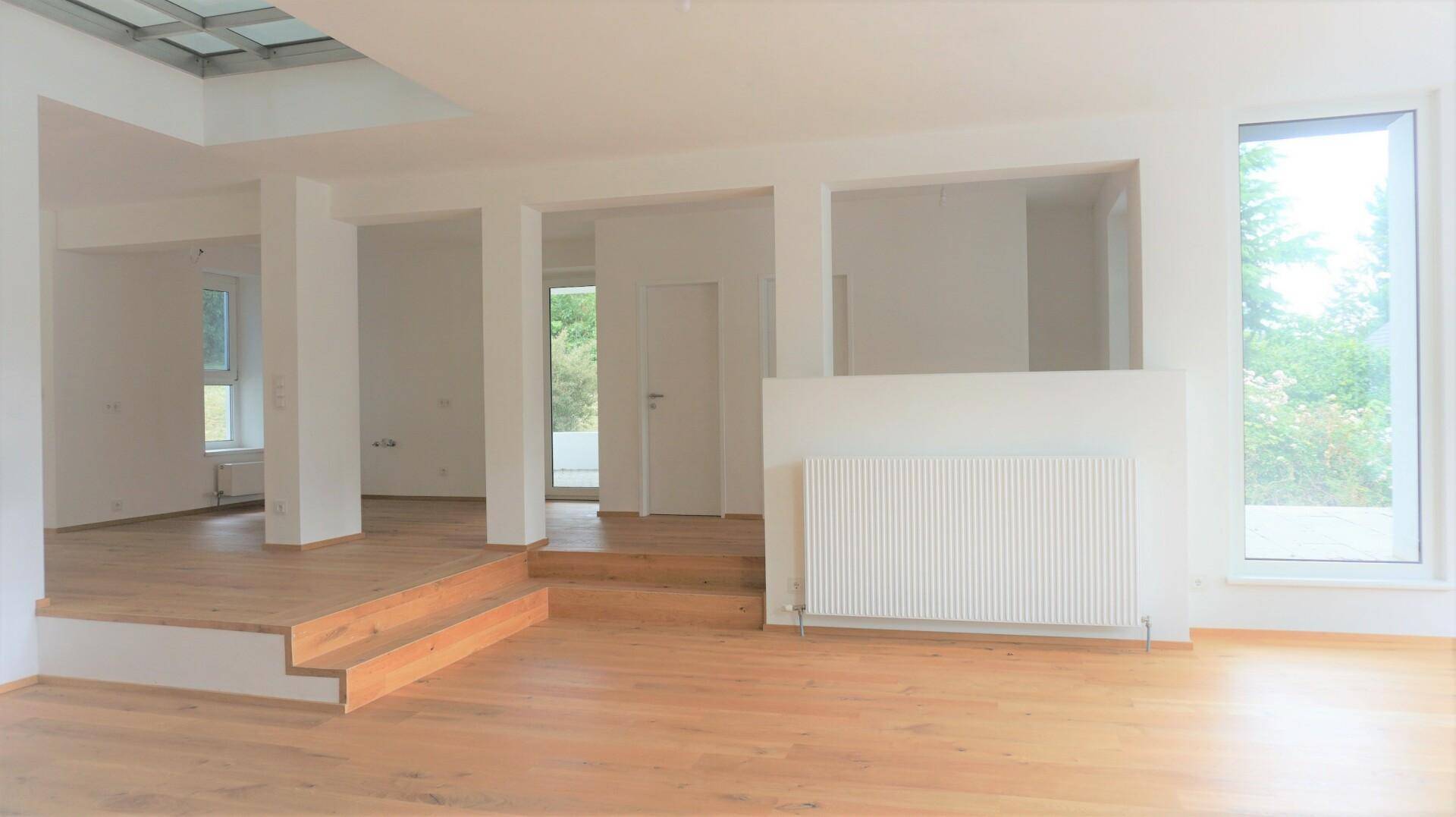 Heller, offener Wohnbereich mit Holzfußboden, großen Fenstern und viel Tageslicht.