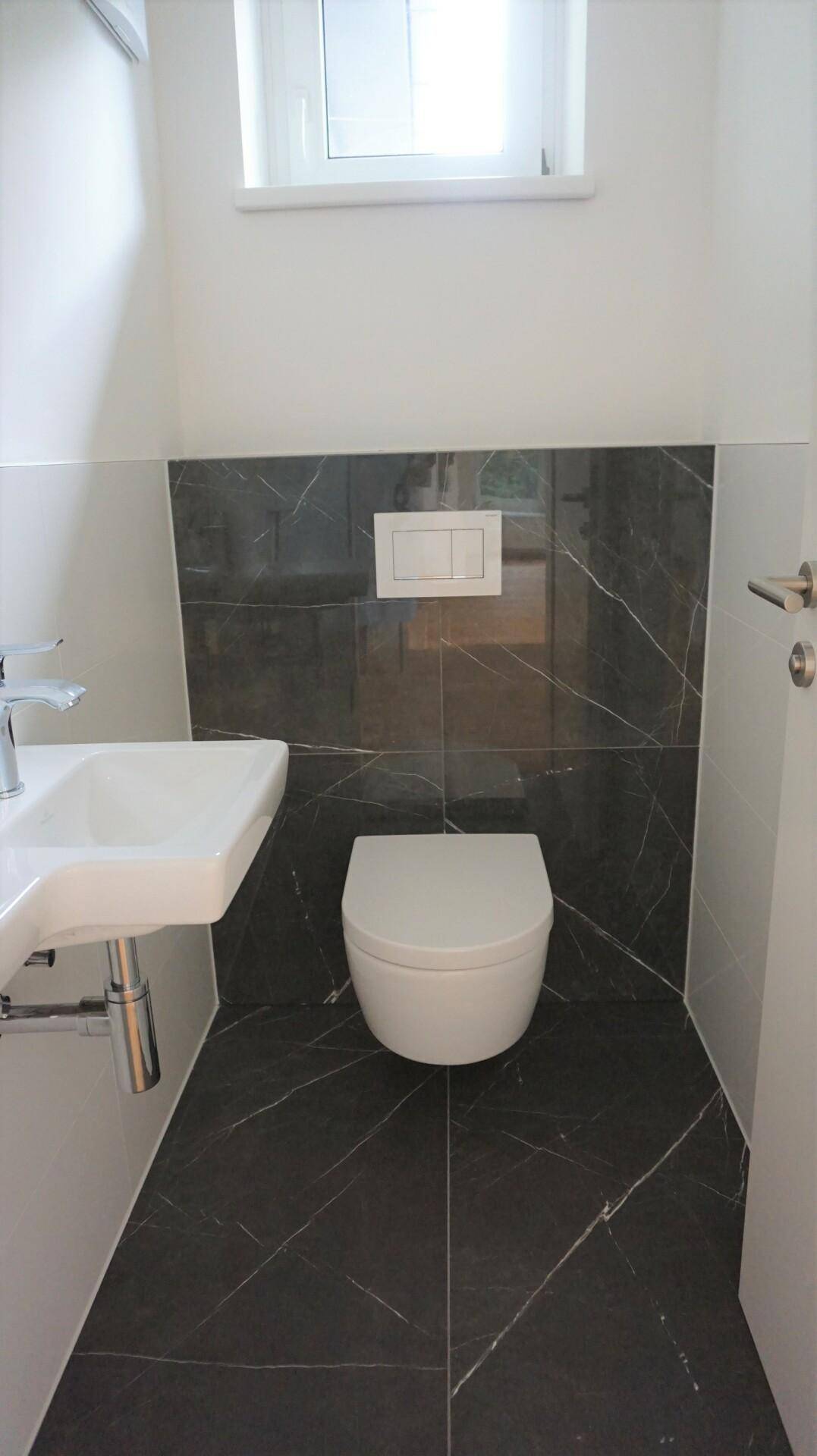 Kleines Gäste-WC mit modernem Wand-WC, kleinem Waschbecken und dunklen Marmorfliesen.