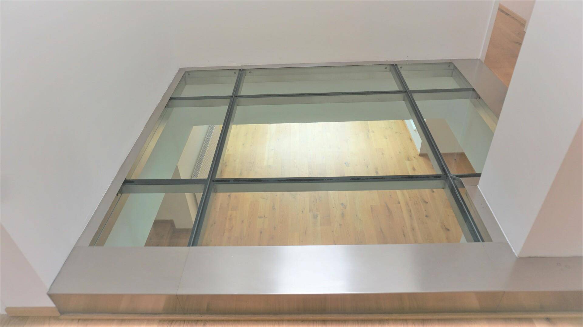 Modernes Designelement mit begehbarer Glasfläche im Boden, das Licht in die darunterliegende Etage lässt.