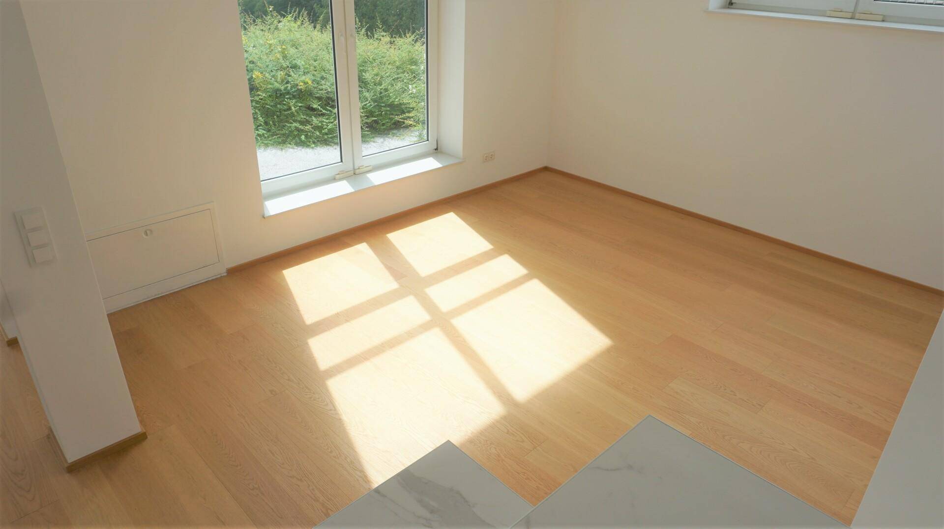 Heller Raum mit Holzfußboden und viel natürlichem Sonnenlicht durch große Fenster.