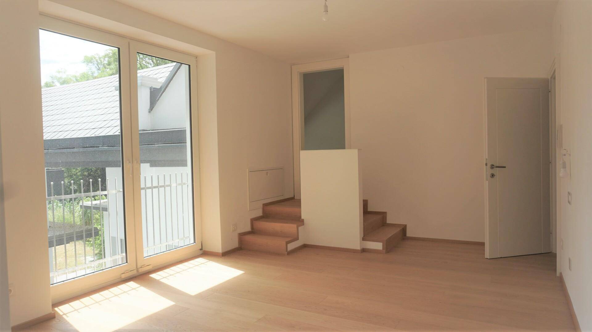 Lichtdurchfluteter Raum mit Zugang zum Balkon und Holztreppe.