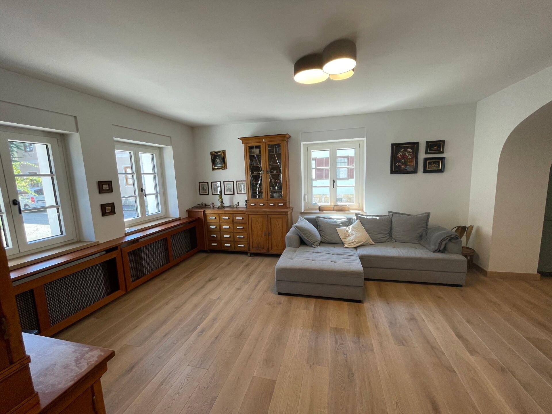 Gemütliches Wohnzimmer mit bequemer Couch, traditionellen Möbeln und großen Fenstern.