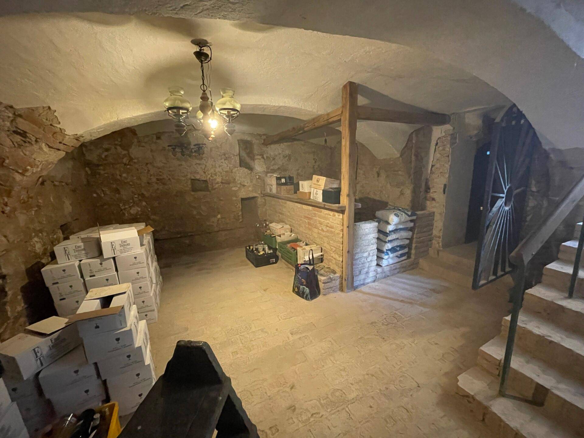 Historischer Keller mit Gewölbedecke, Steinmauern und Lagerflächen für Wein oder Güter.