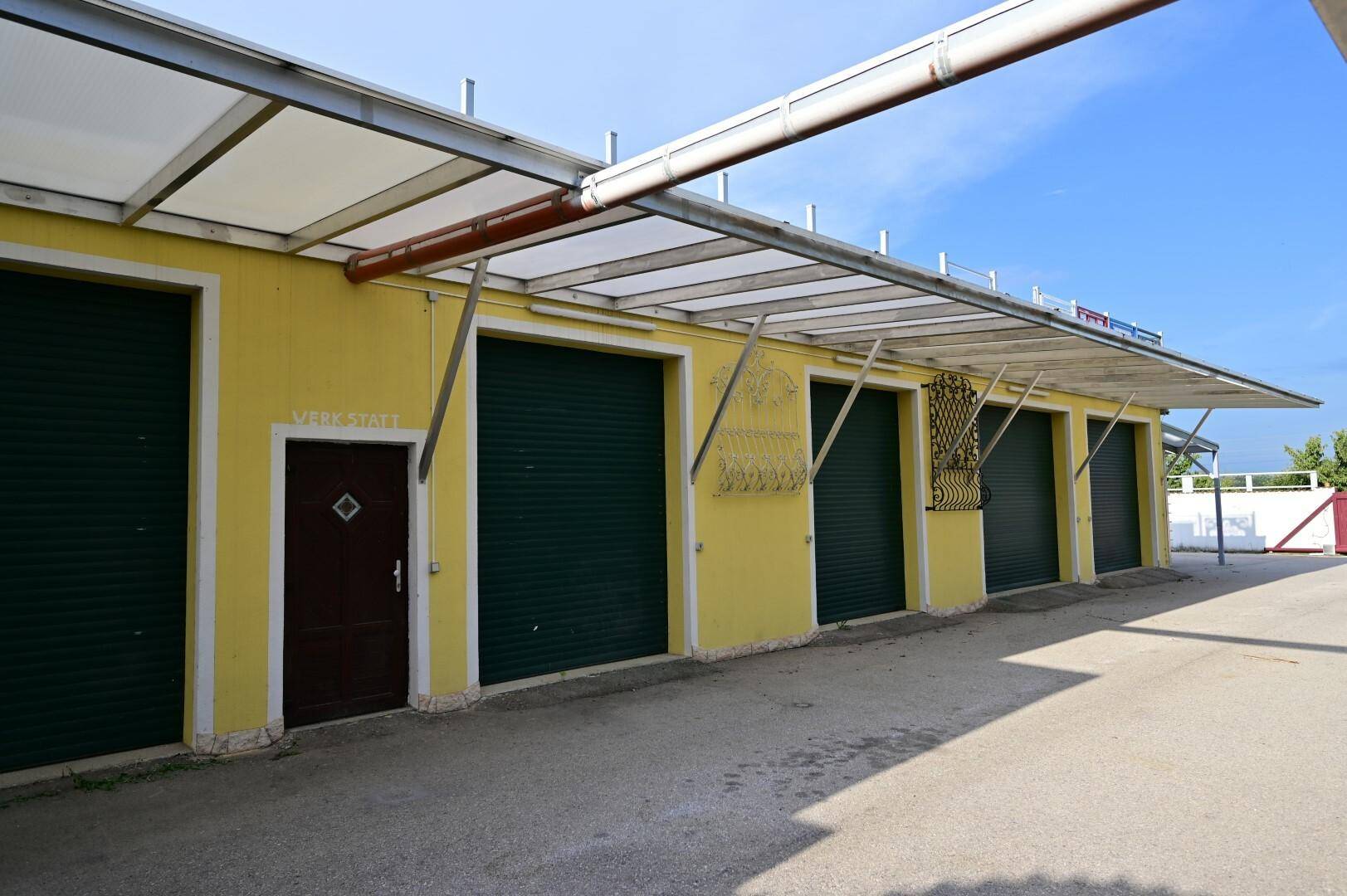 Nebengebäude mit mehreren Garagentoren und einem überdachten Vordach, ideal für Lager oder Werkstätten mit direktem Zugang.