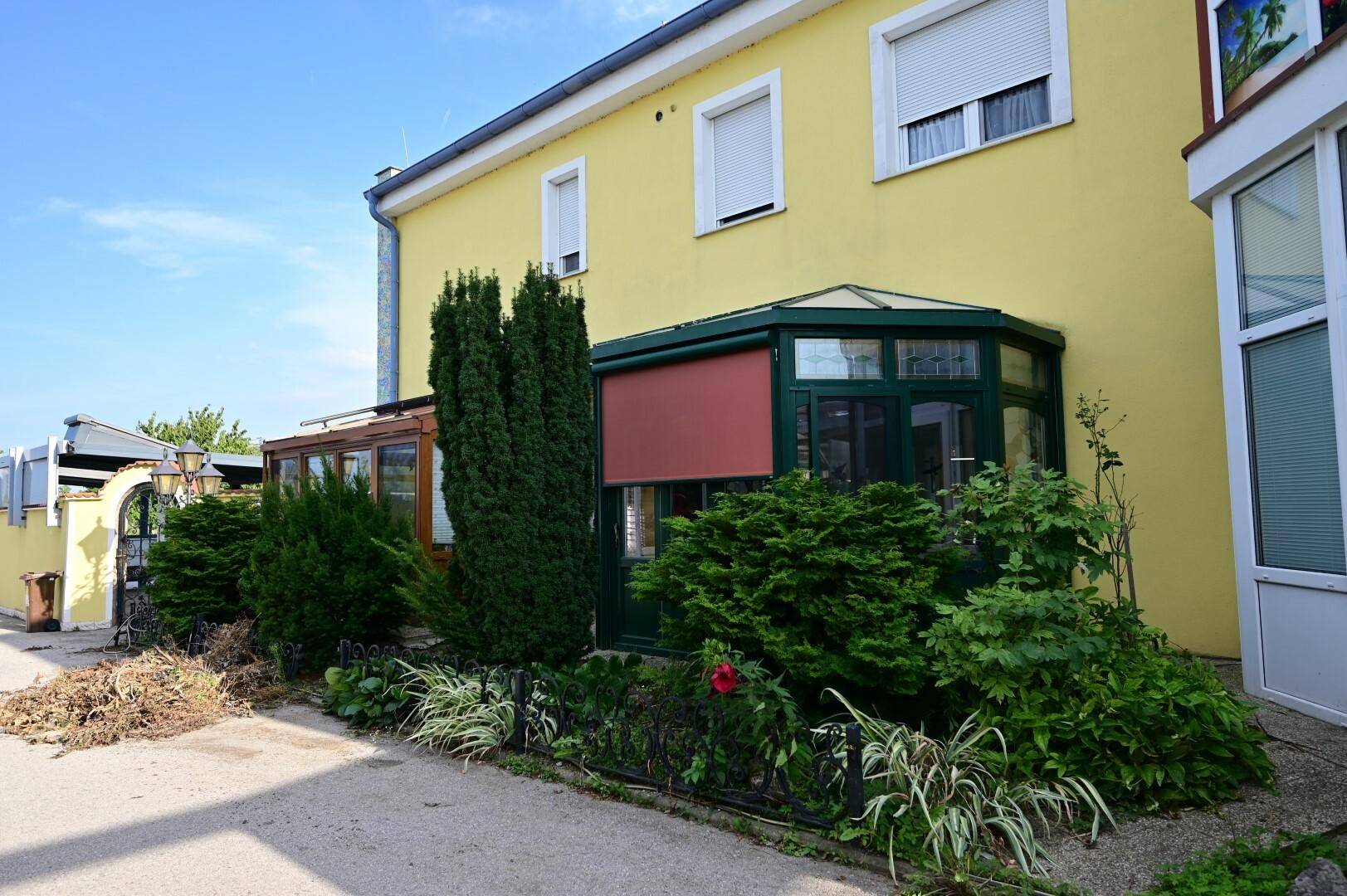 Seitenansicht des Gebäudes mit einem kleinen, gepflegten Gartenbereich und einem Wintergartenanbau, der zum Entspannen einlädt.