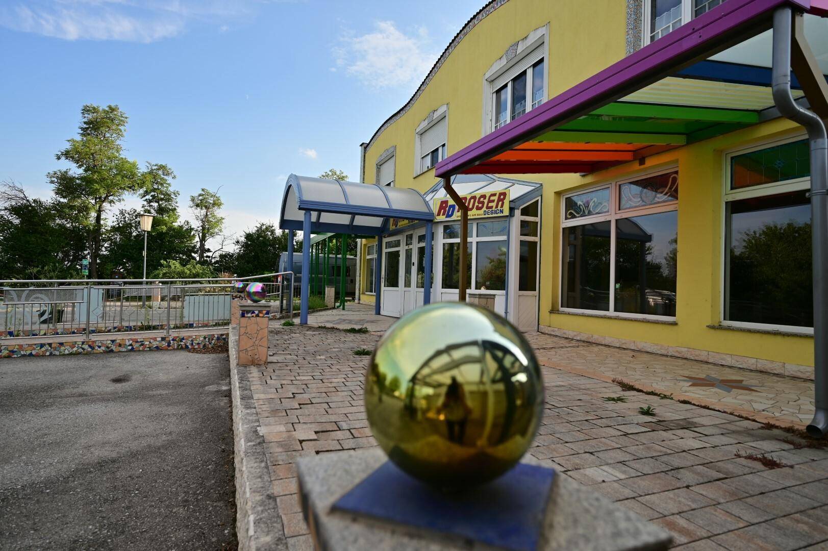 Vorderansicht des Gebäudes mit Eingangsbereich und einer dekorativen goldenen Kugel im Vordergrund, die das Anwesen schmückt.
