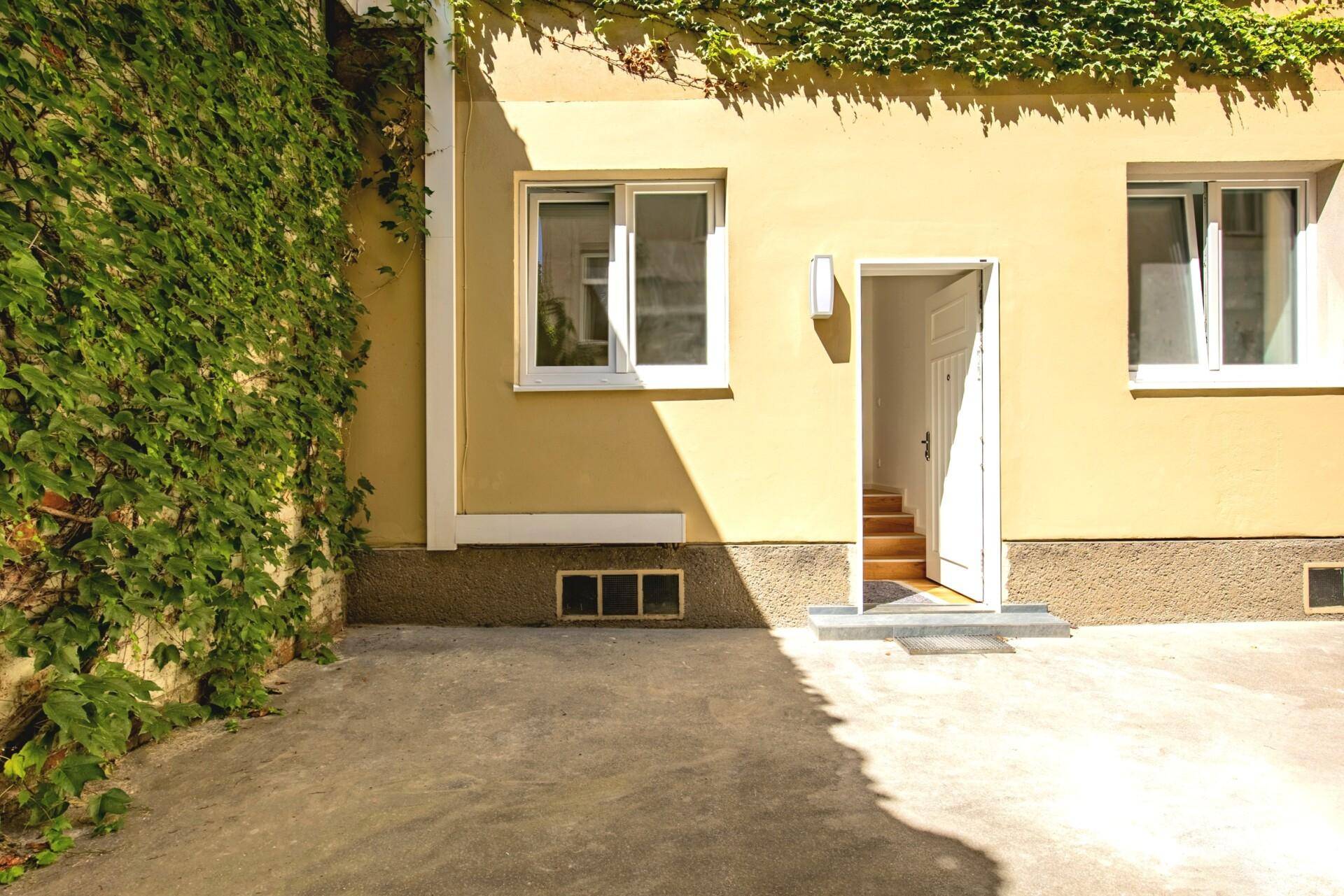 Fassade eines Gebäudes mit Fenstern, offener Tür und üppigem Efeu, das die Wand bedeckt.