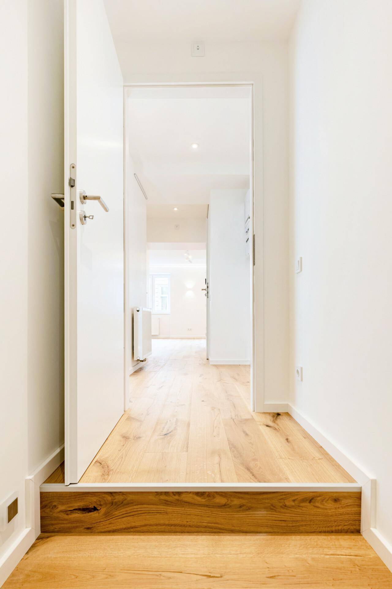 Heller Flur mit Holzboden und weiß gestrichenen Wänden, führt zu weiteren Räumen der Wohnung.