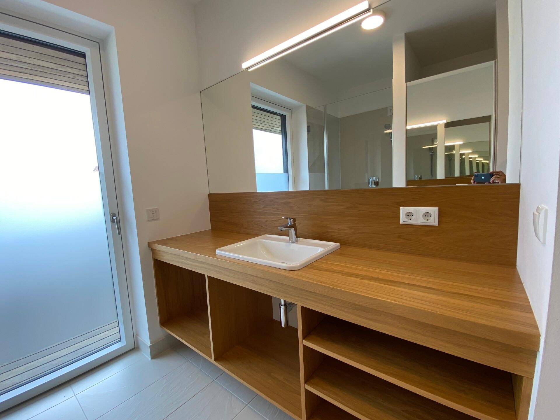 Modernes Badezimmer mit Holzwaschtisch, großem Spiegel und Fenster für Tageslicht.