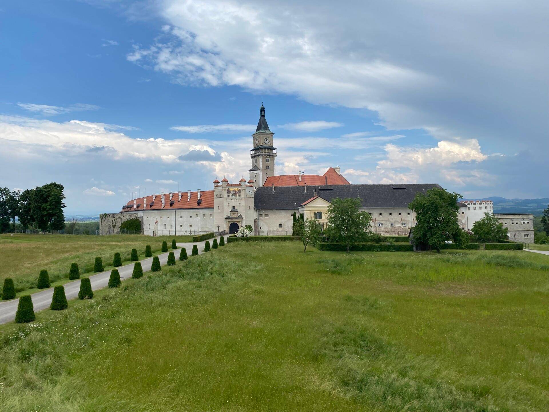 Historische Schlossanlage mit weitläufigen Grünflächen unter einem bewölkten Himmel.