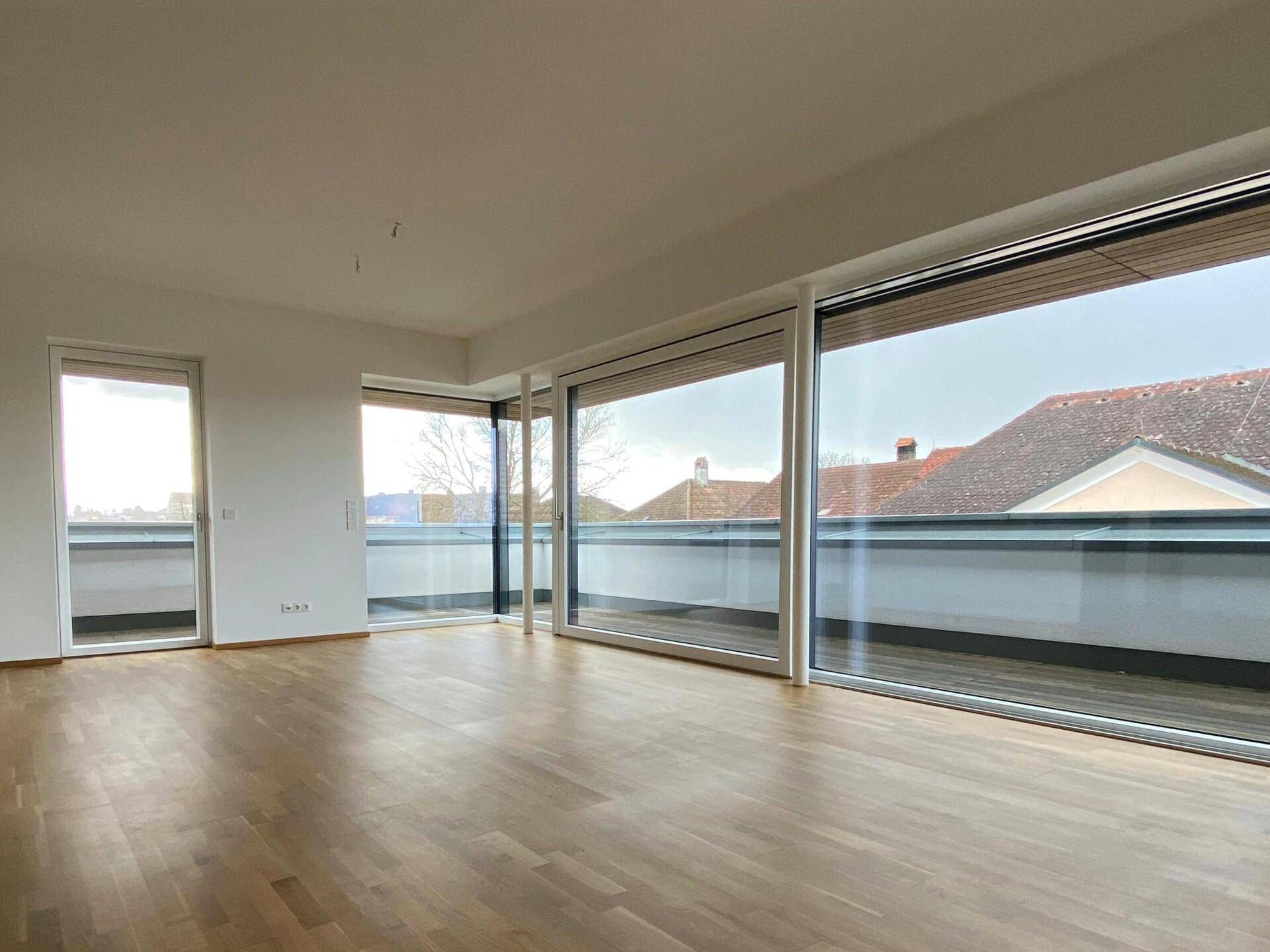 Heller Wohnraum mit Eichenparkett und großen Fensterfronten, die viel Tageslicht hereinlassen.
