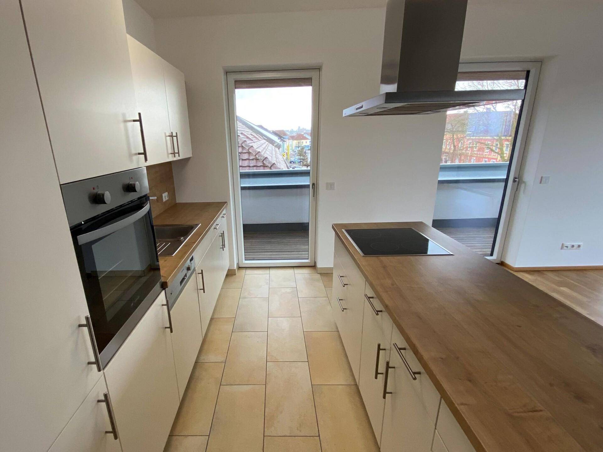 Helle Küche mit weißen Schränken, Holzarbeitsplatte und direktem Zugang zu einem Balkon.