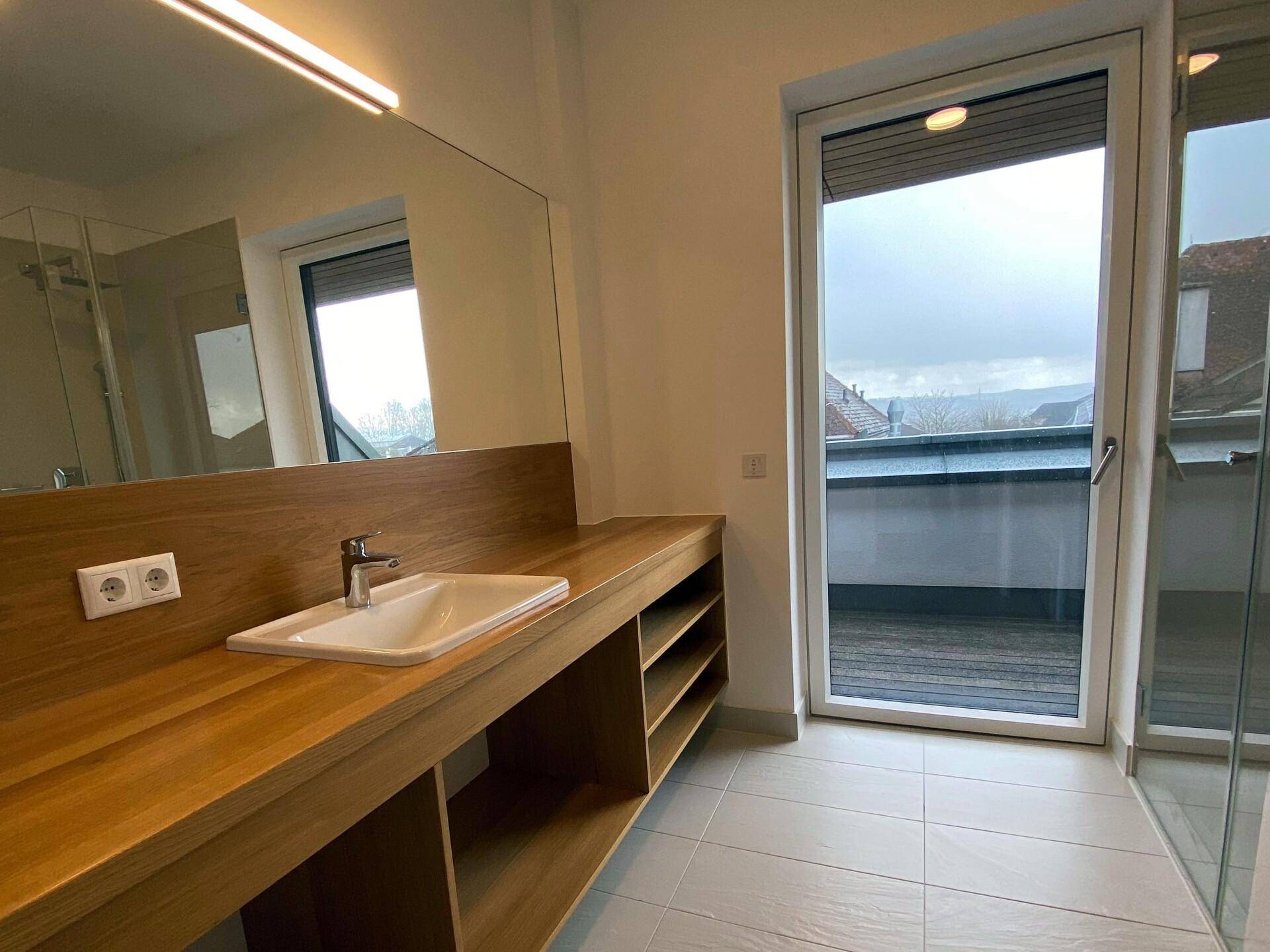 Modernes Badezimmer mit Holzwaschtisch, großem Spiegel und Fenster mit Blick nach draußen.