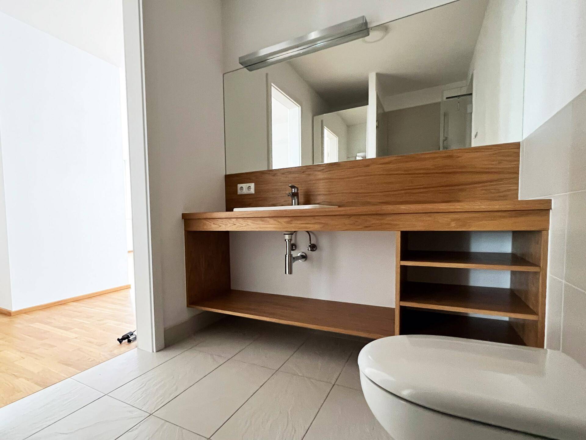 Modernes Badezimmer mit Holzwaschtisch, großem Spiegel und Wand-WC.