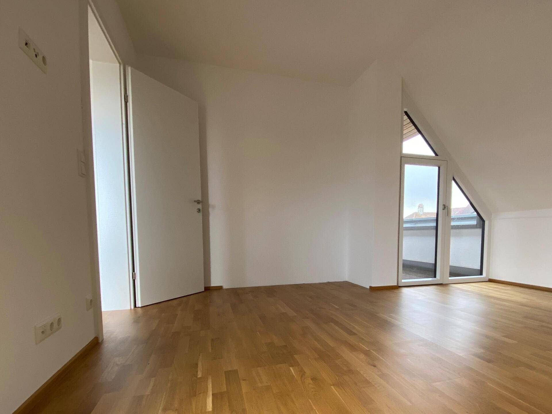 Helles Schlafzimmer im Dachgeschoss mit Holzboden, schrägen Wänden und Zugang zum Balkon.