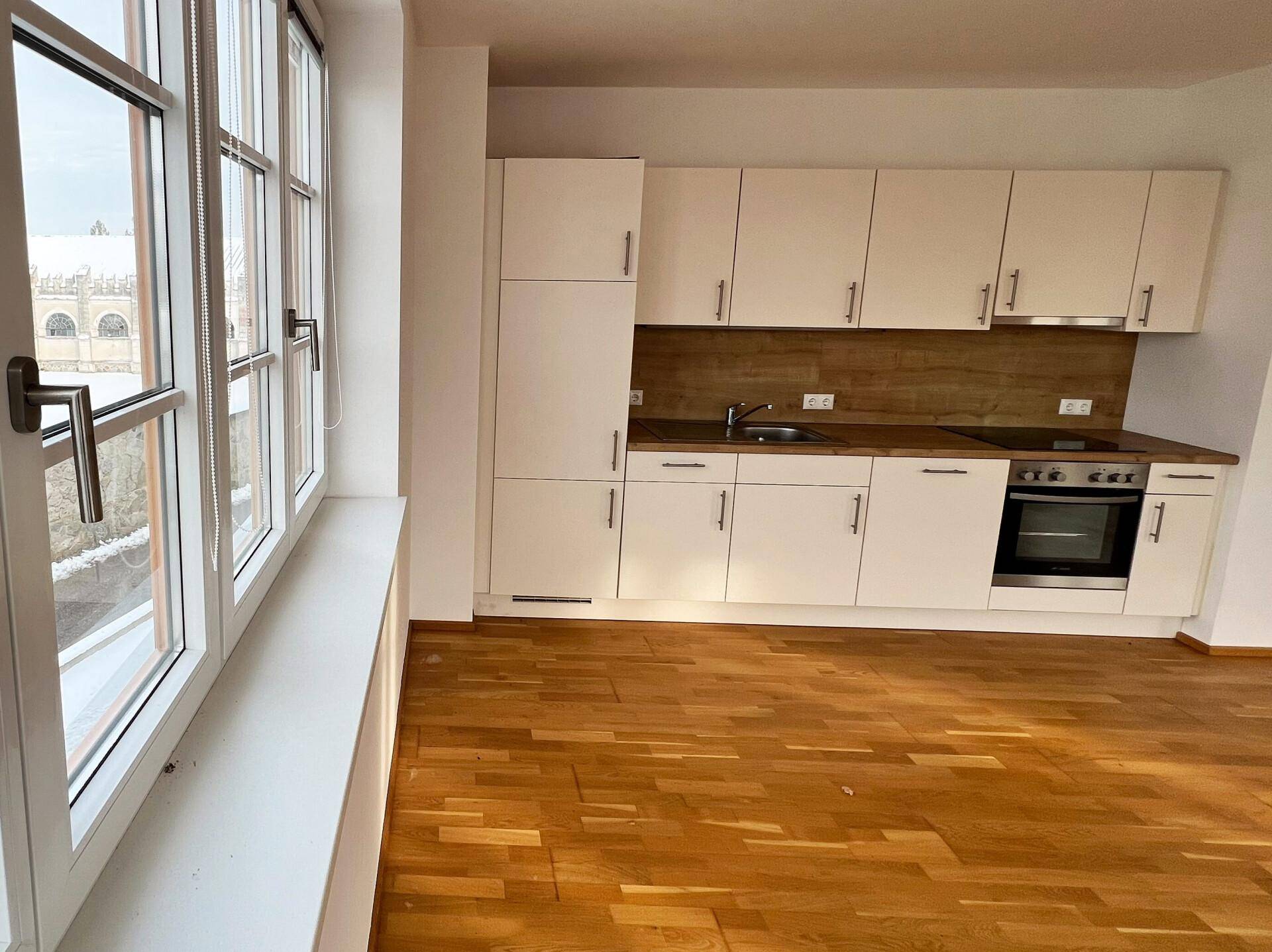 Helle Küche mit weißen Schränken, Holzarbeitsplatte und großem Fenster, das viel Tageslicht hereinlässt.