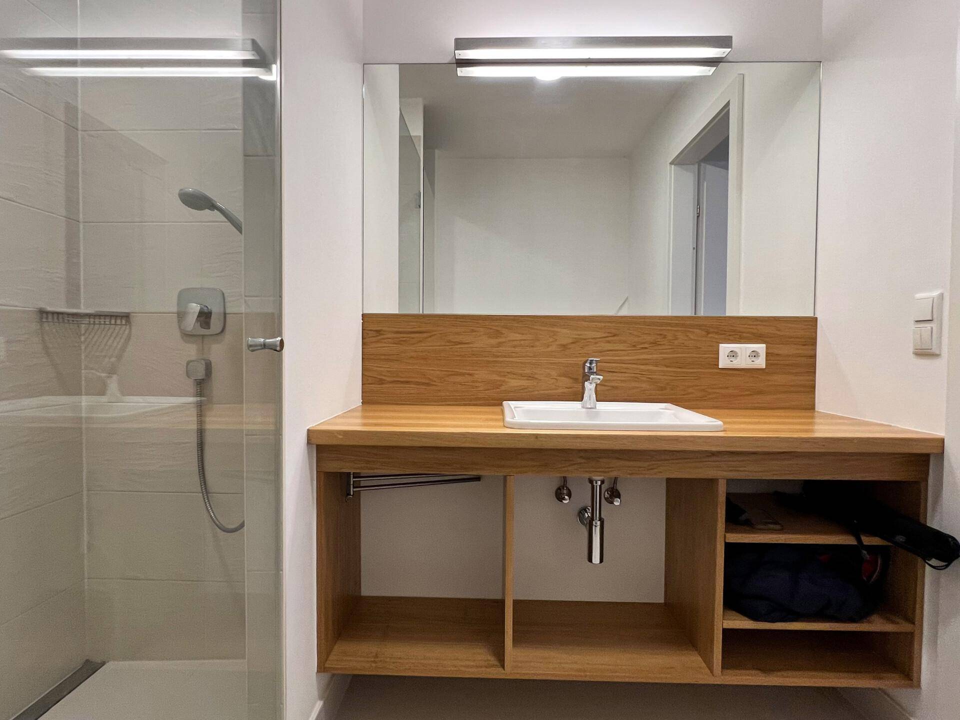 Modernes Badezimmer mit begehbarer Dusche, Holzwaschtisch und großem Spiegel.
