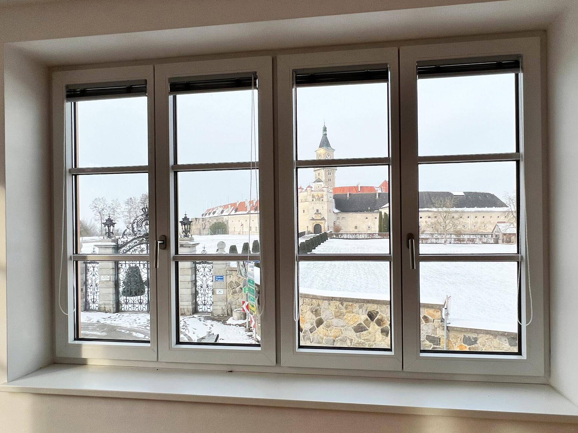 Fensterblick auf ein historisches Schloss in einer verschneiten Winterlandschaft mit weitem Ausblick.