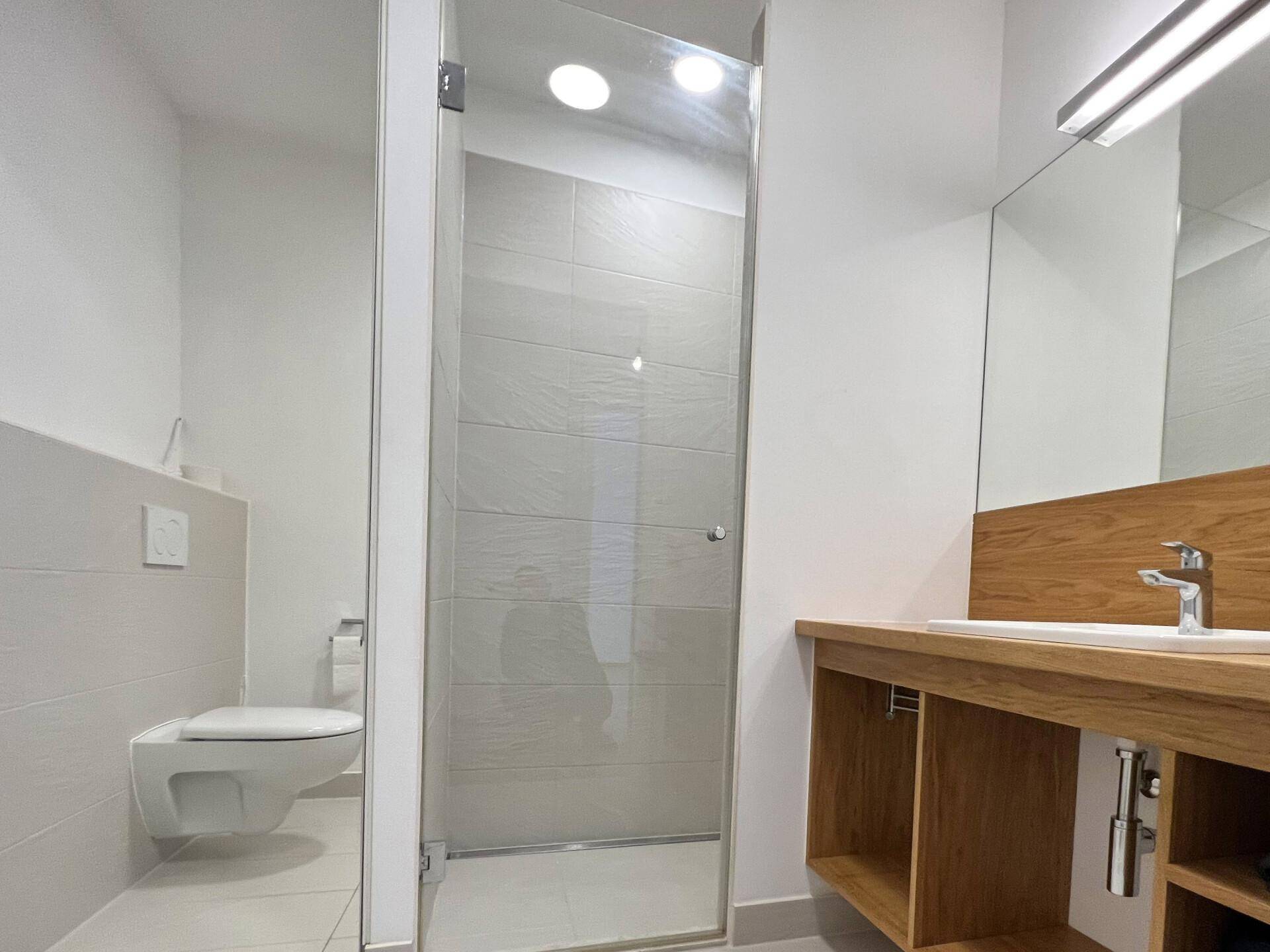 Modernes Badezimmer mit begehbarer Dusche, wandhängendem WC und Holzwaschtisch mit Einzelwaschbecken.