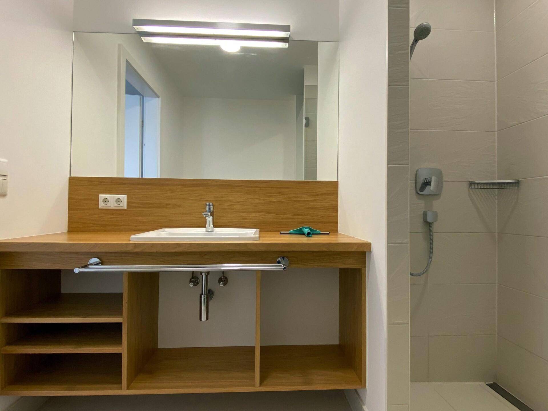 Badezimmer mit Holzwaschtisch, Einzelwaschbecken, großem Spiegel und Duscharmatur.