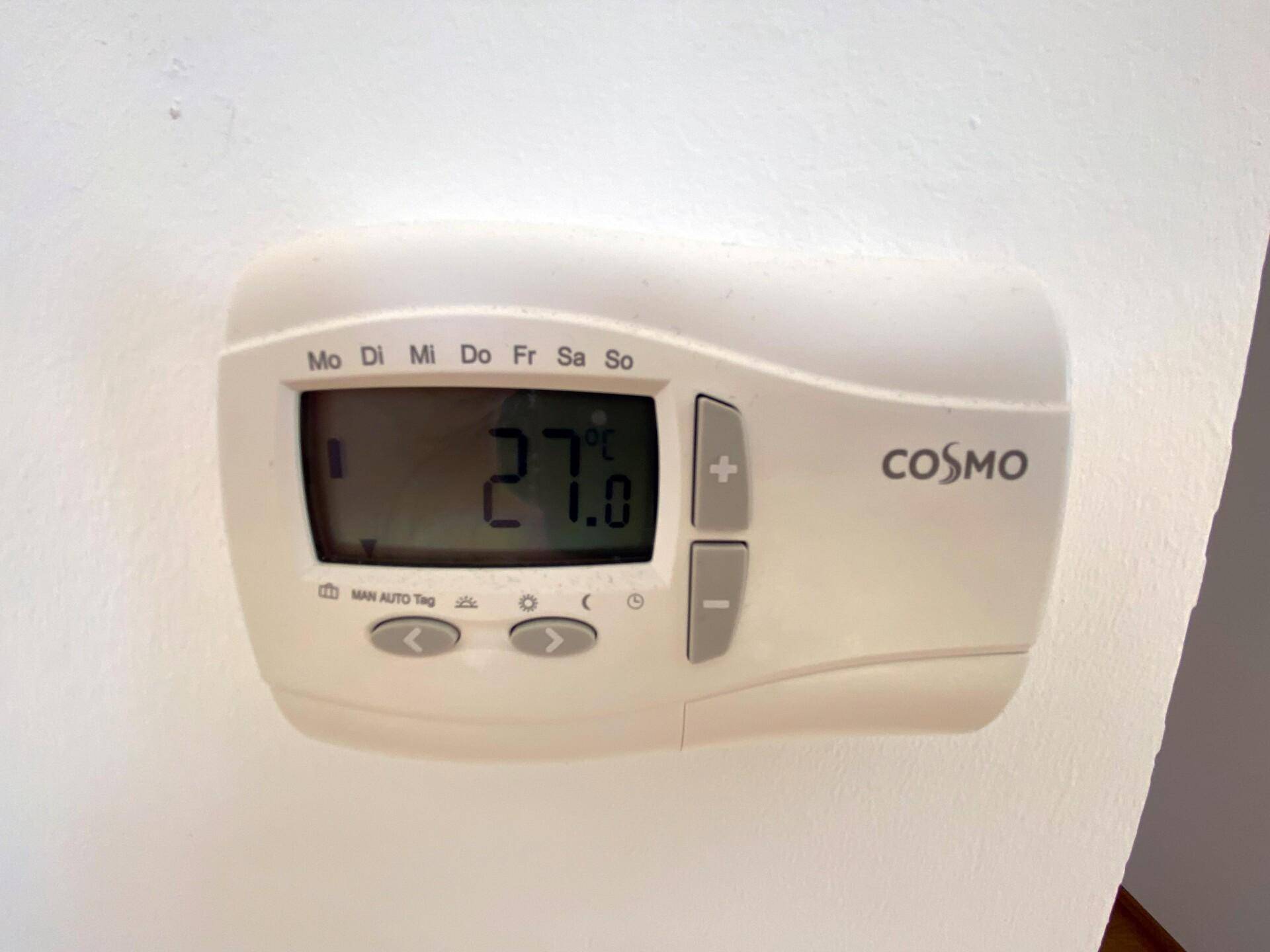Nahaufnahme eines modernen digitalen Thermostats der Marke Cosmo an einer weißen Wand.