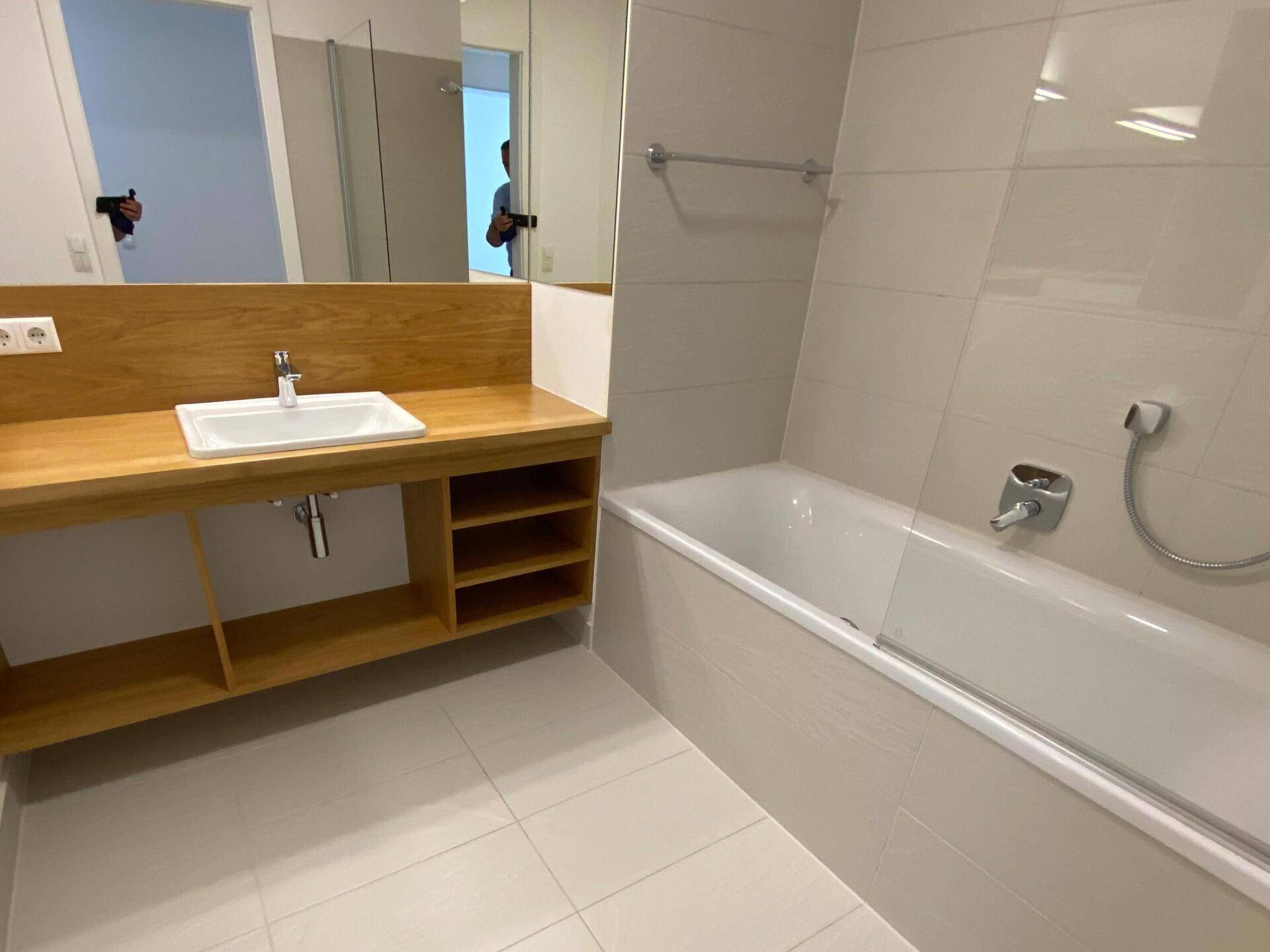 Modernes Badezimmer mit Badewanne, Holzwaschtisch, Einzelwaschbecken und großem Spiegel.