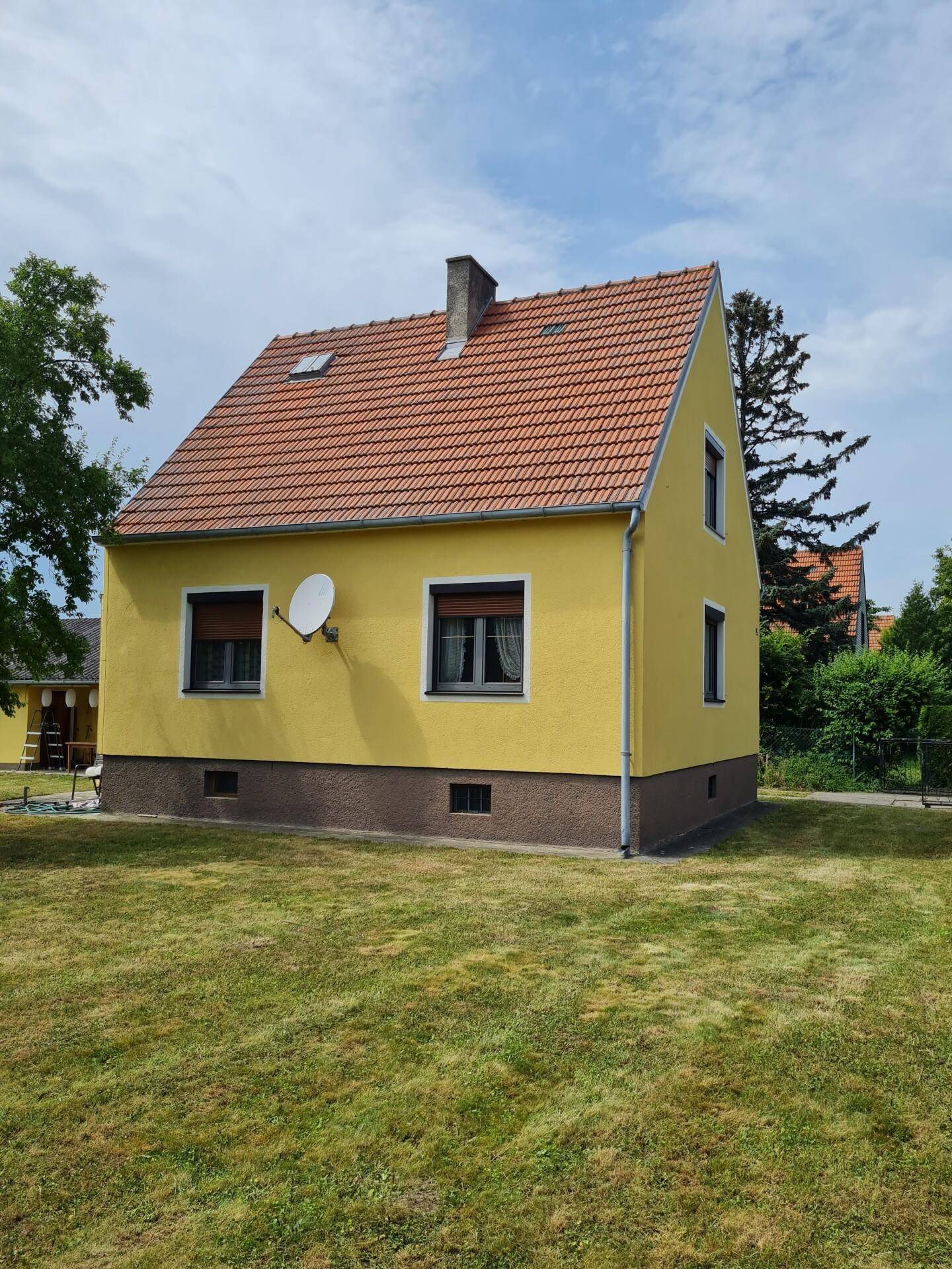 Gelbes Einfamilienhaus mit rotem Ziegeldach und Rollläden an den Fenstern.