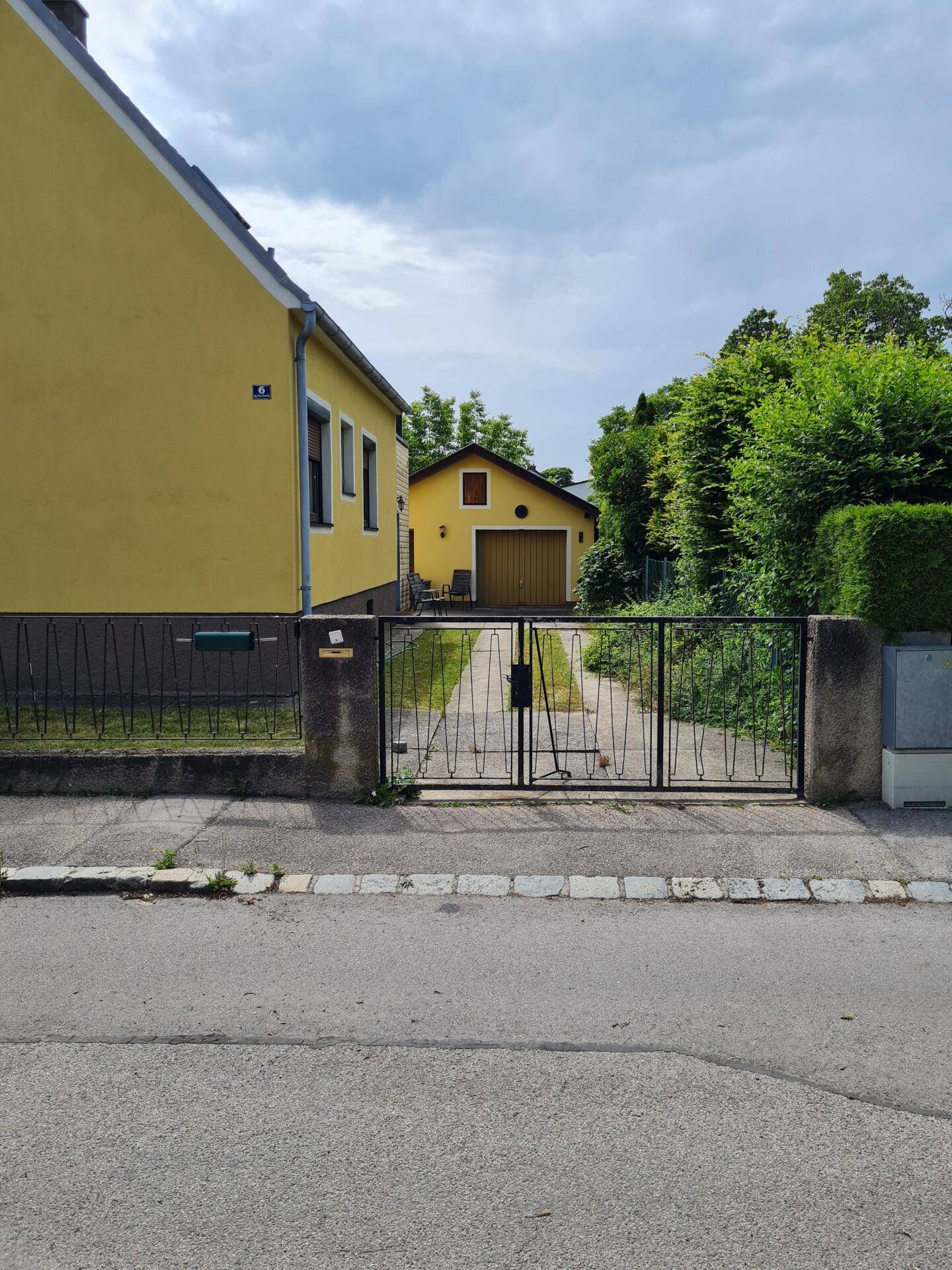 Einfahrt zum Grundstück mit Metalltor und Blick auf das gelbe Haus und die Garage.