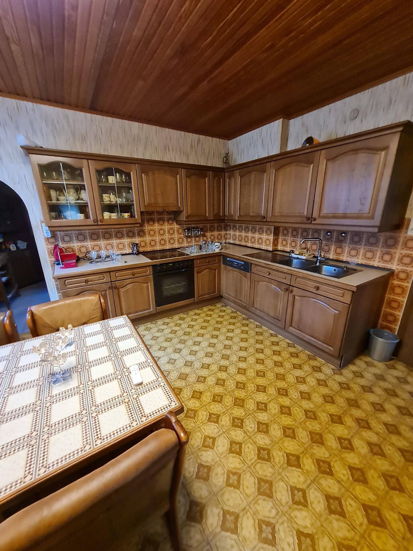 Traditionelle Holzküche mit gemusterten Fliesen und Esstisch, unter einer Holzdecke.