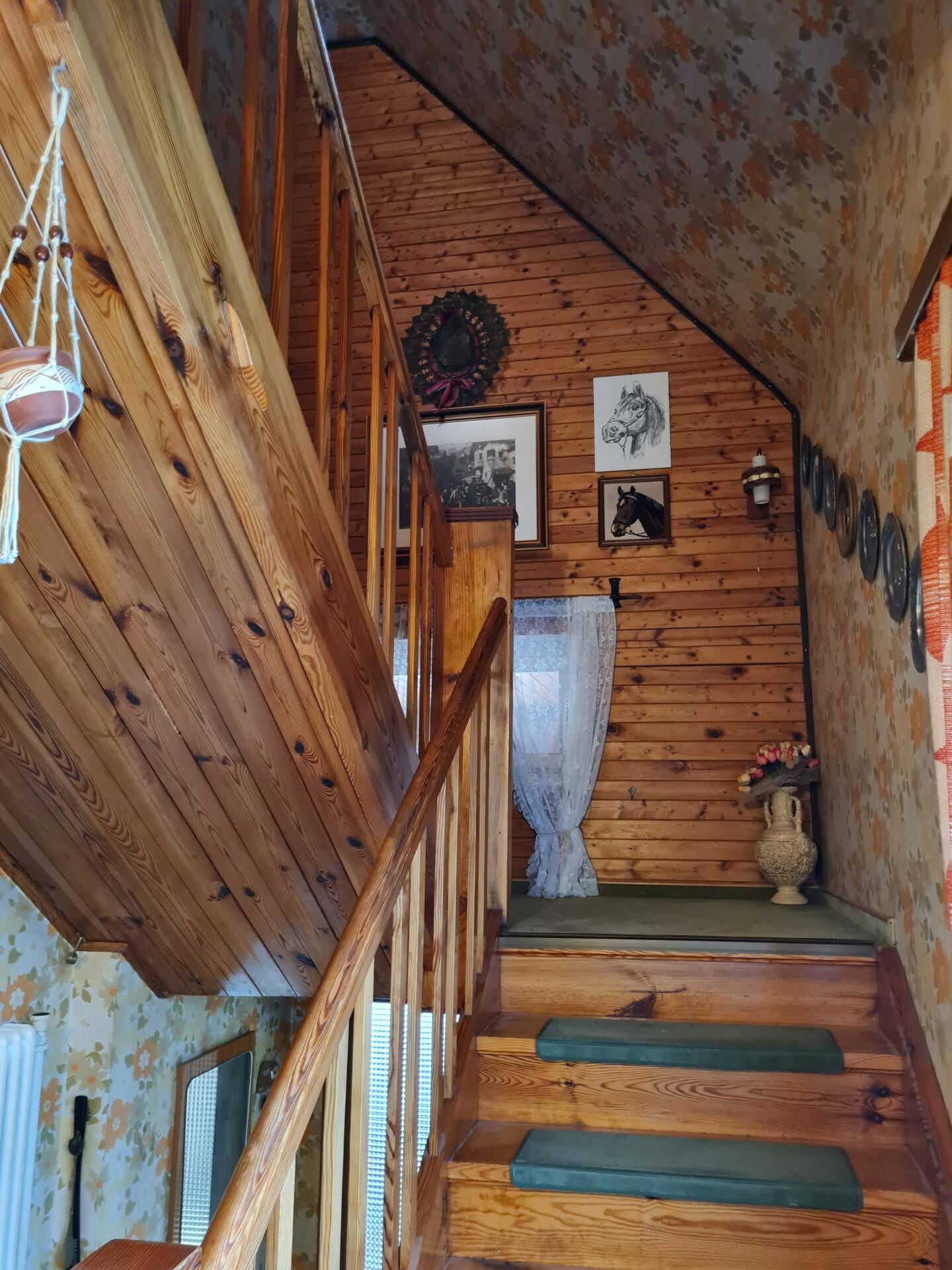 Holztreppe mit Geländer und floraler Tapete führt in die obere Etage.